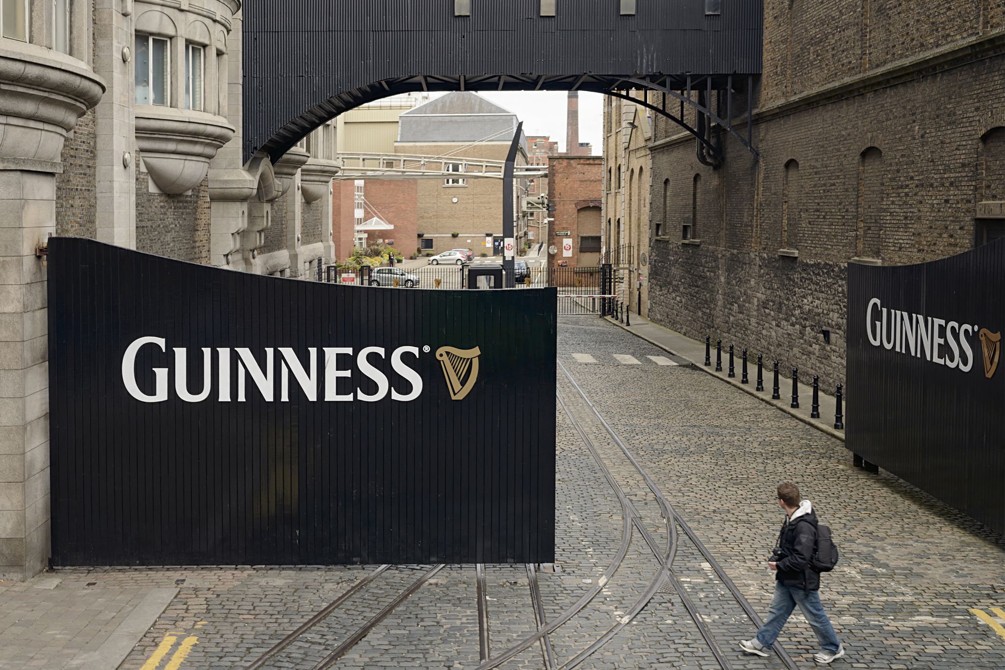 A man walking past large entrance gates to the St. James's Gate Brewery in Dublin