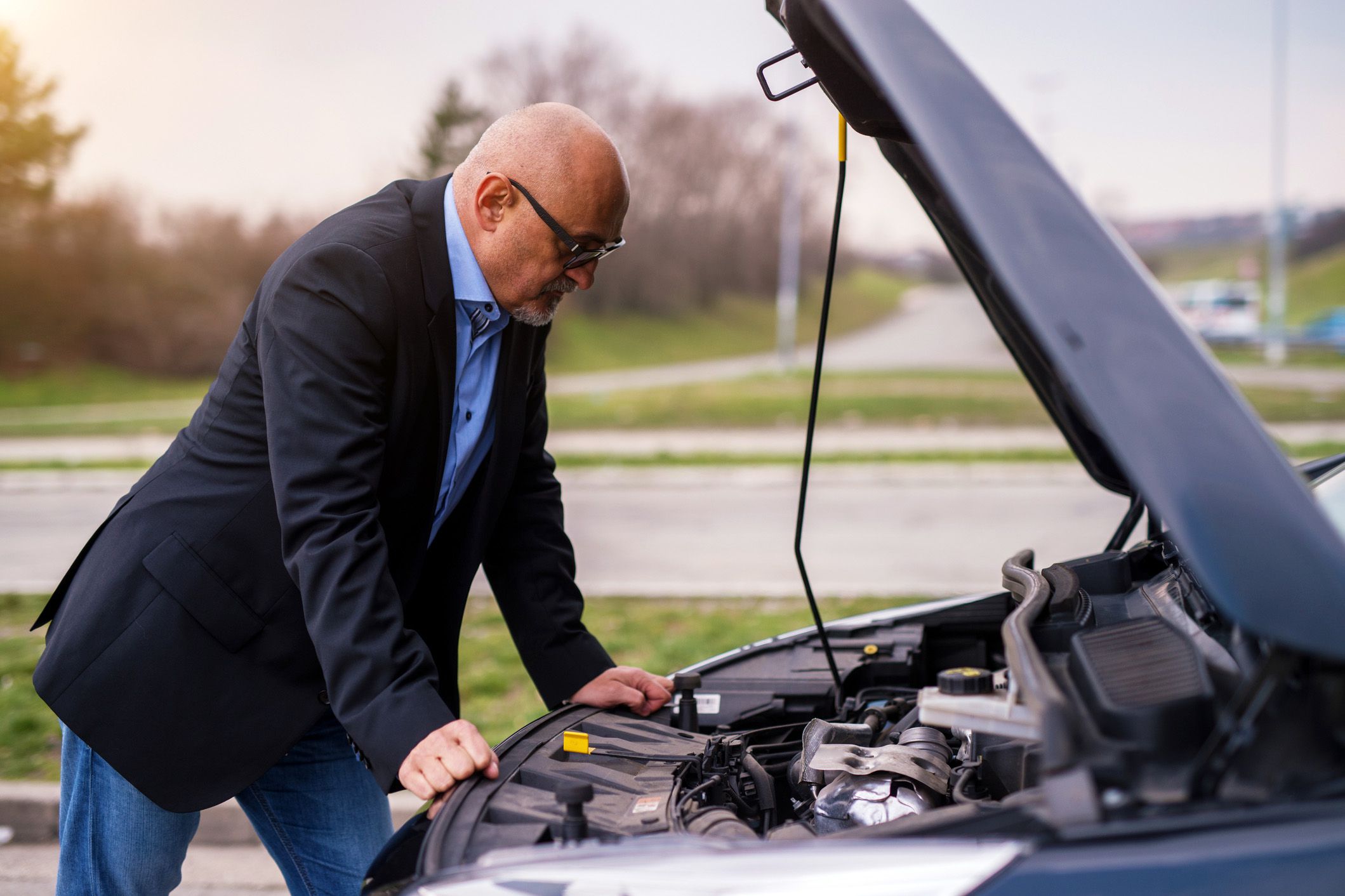 man looking under car hood on side of road