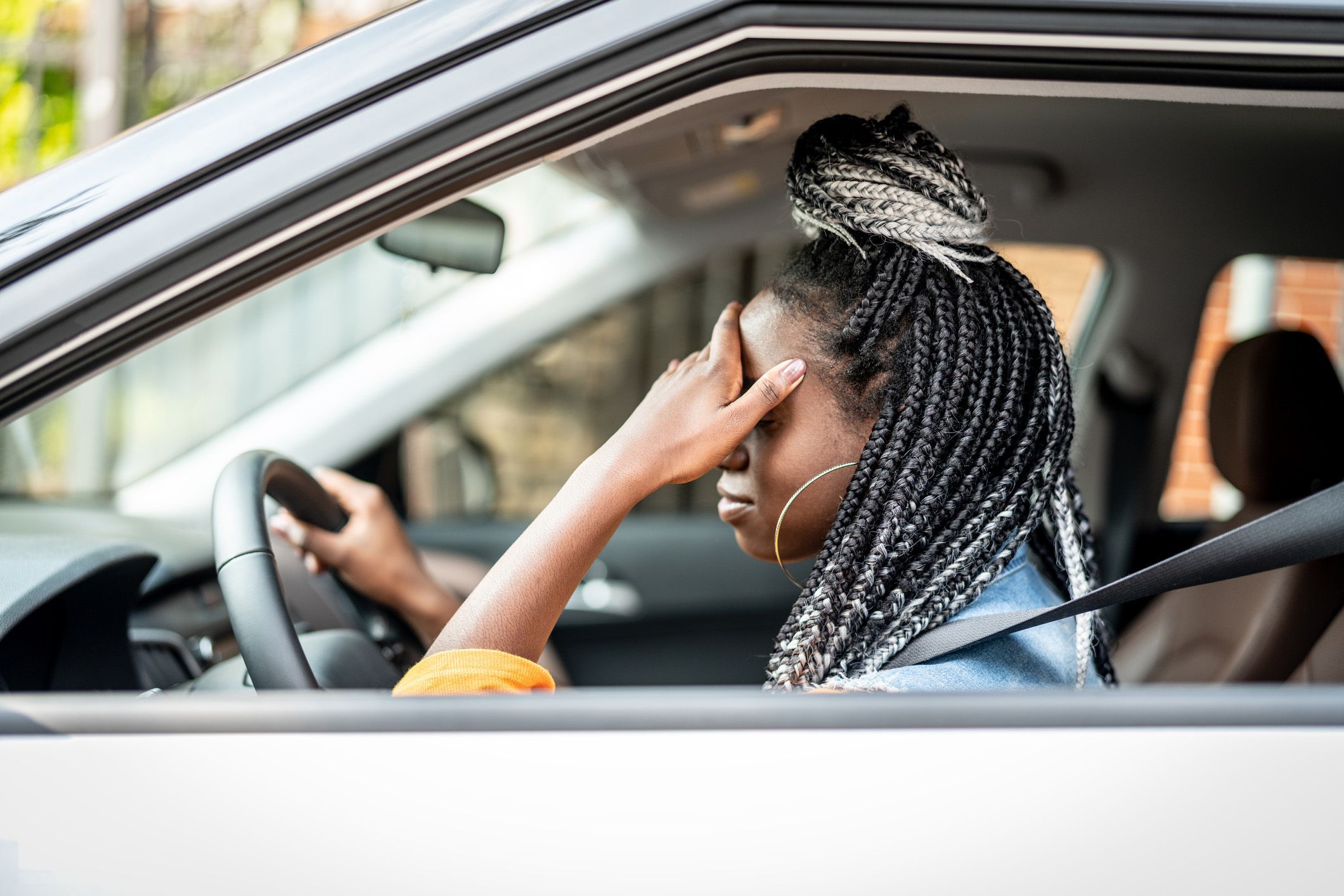 tired woman in car with head in hand