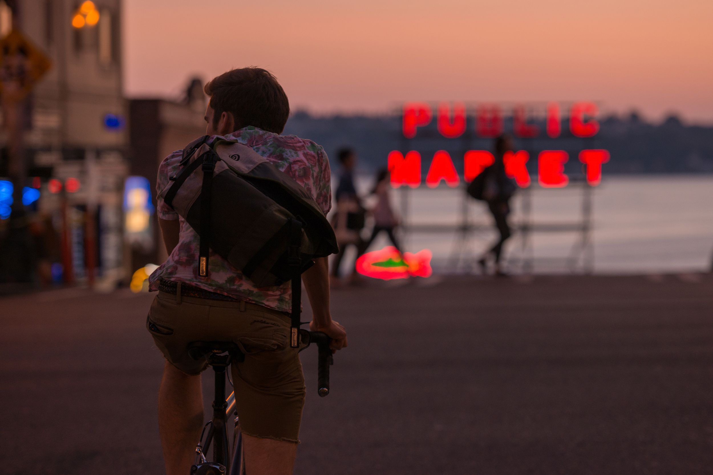 man on bike in front of Pike Place Public Market sign at sunset