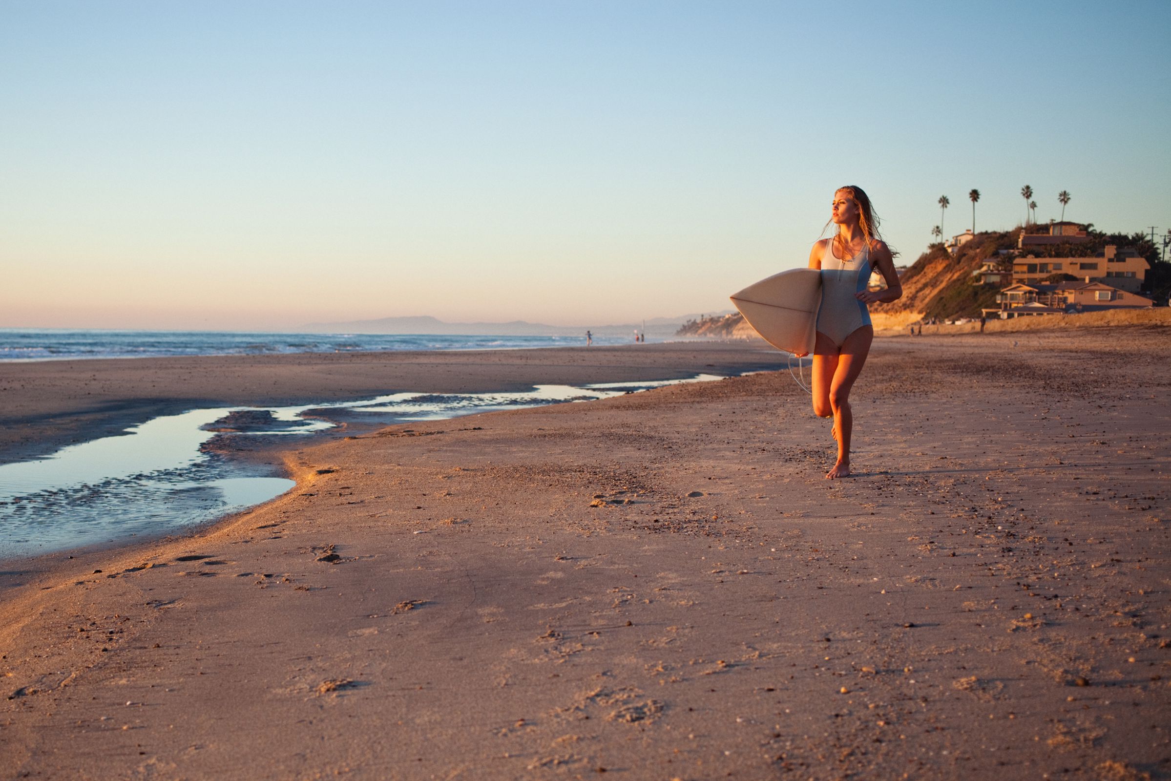 surfer girl holding surf board while jogging on beach of San Diego