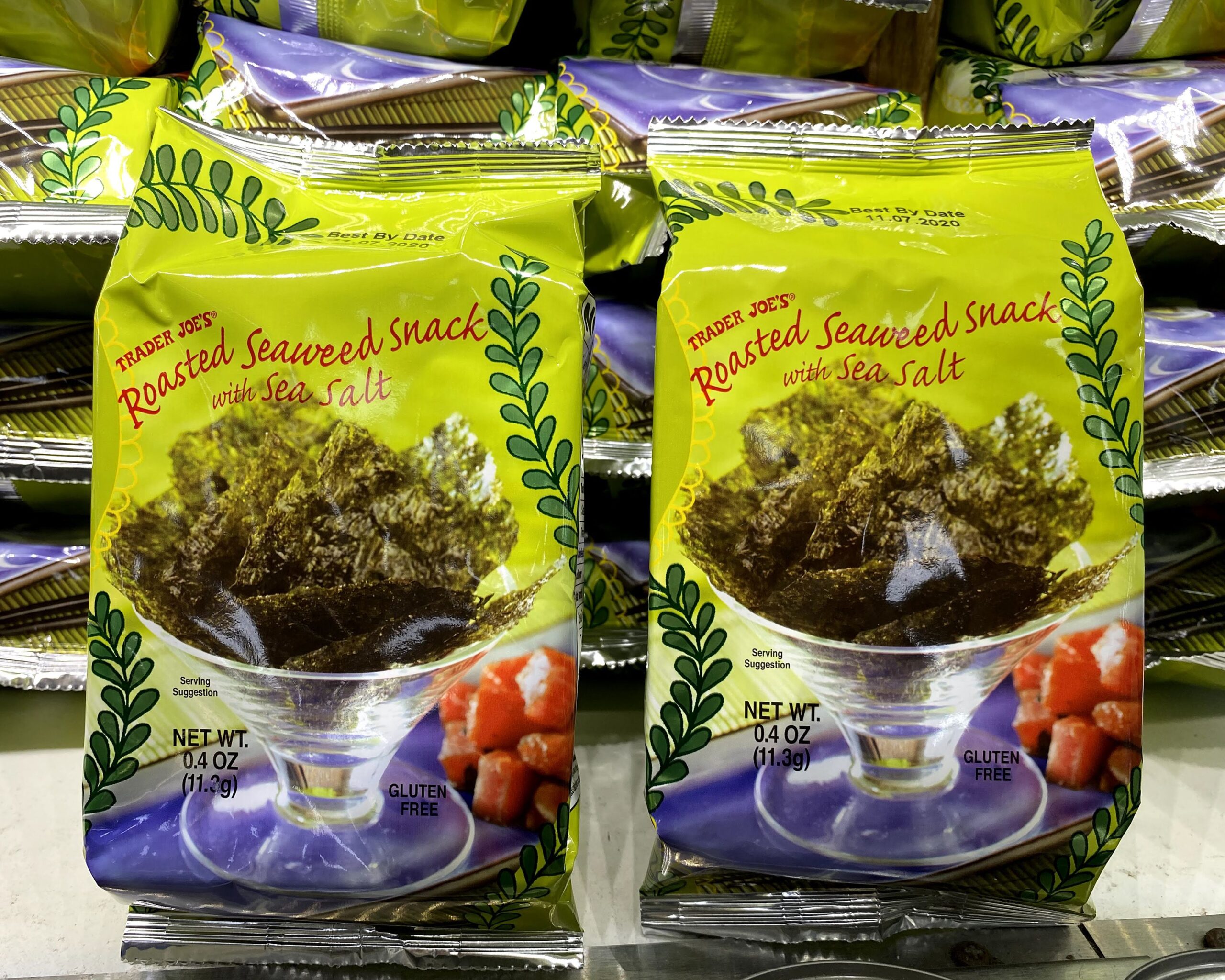 Two bags of Trader Joe's Roasted Seaweed Snack at a Trader Joe's, on a beige shelf in front of organized piles of more bags