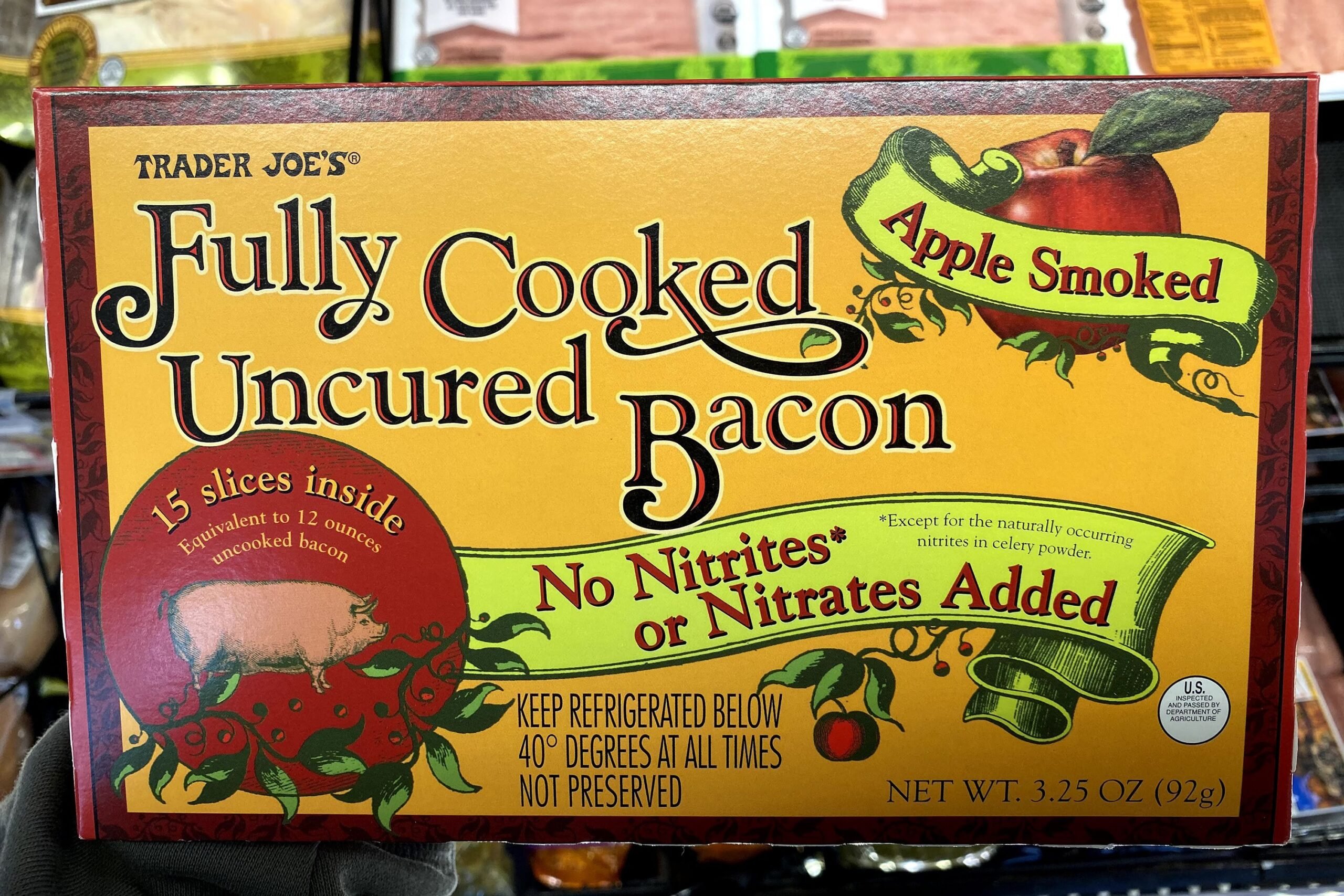 Box of Trader Joe's Full Cooked Uncured Bacon at a Trader Joe's, meats blurred in the background