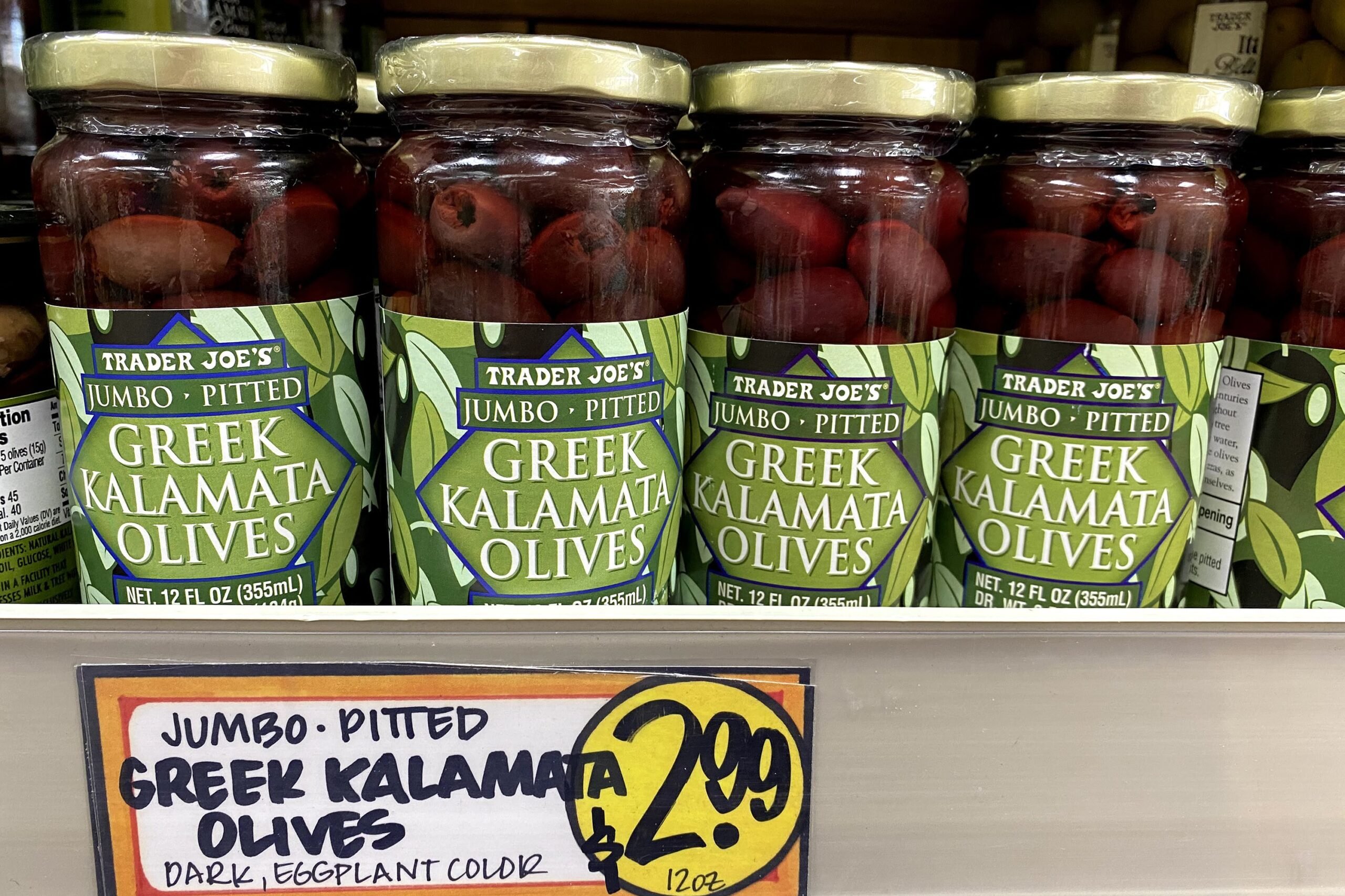 Jars of Trader Joe's Greek Kalamata Olives at a Trader Joe's, on a shelf, a fun sign in the foreground