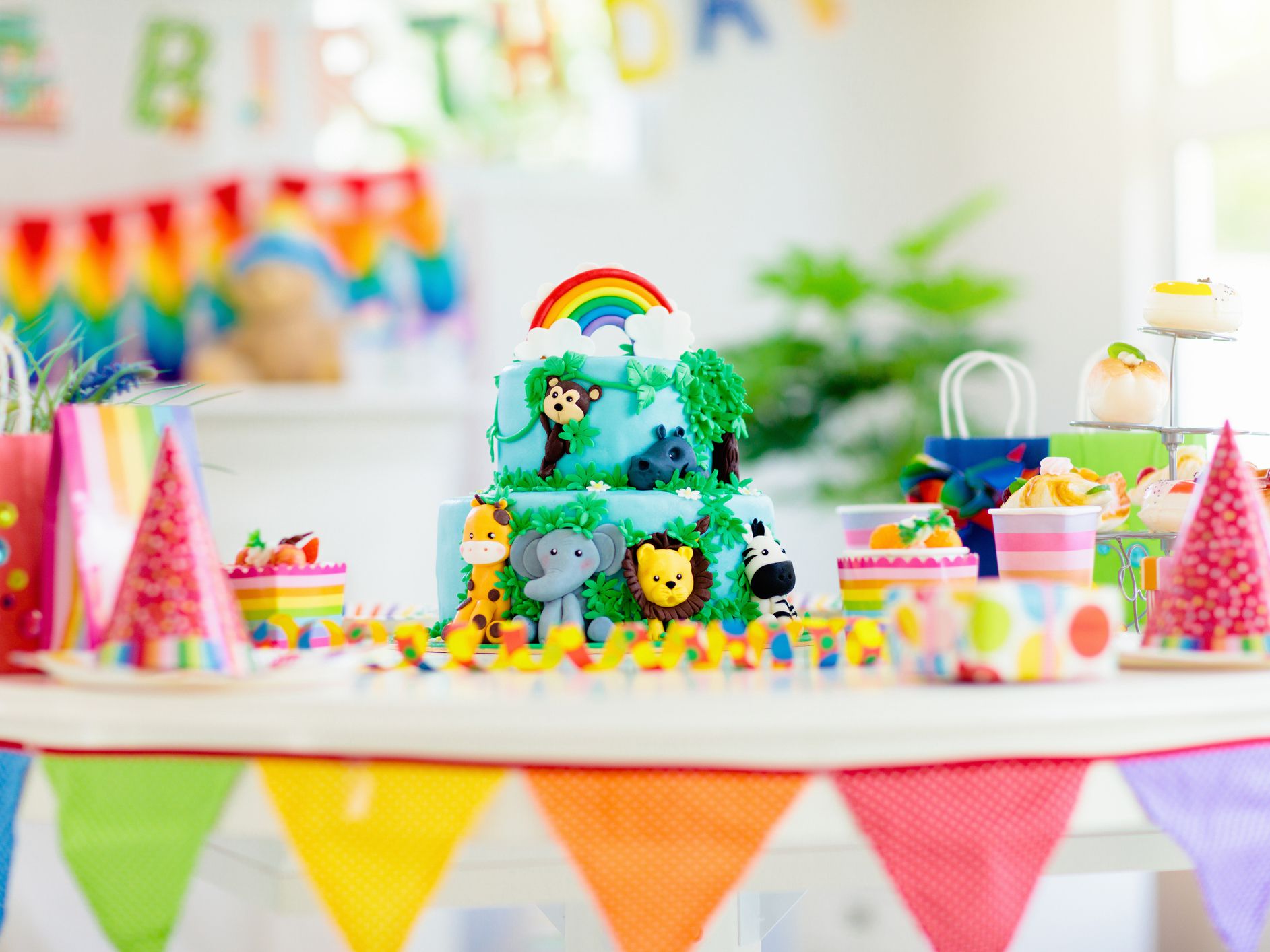 Cake for kids birthday celebration. Jungle animals theme children party. Decorated room for boy or girl kid birthday. Table setting with presents, gift boxes, confetti and sweets. Pastry for child