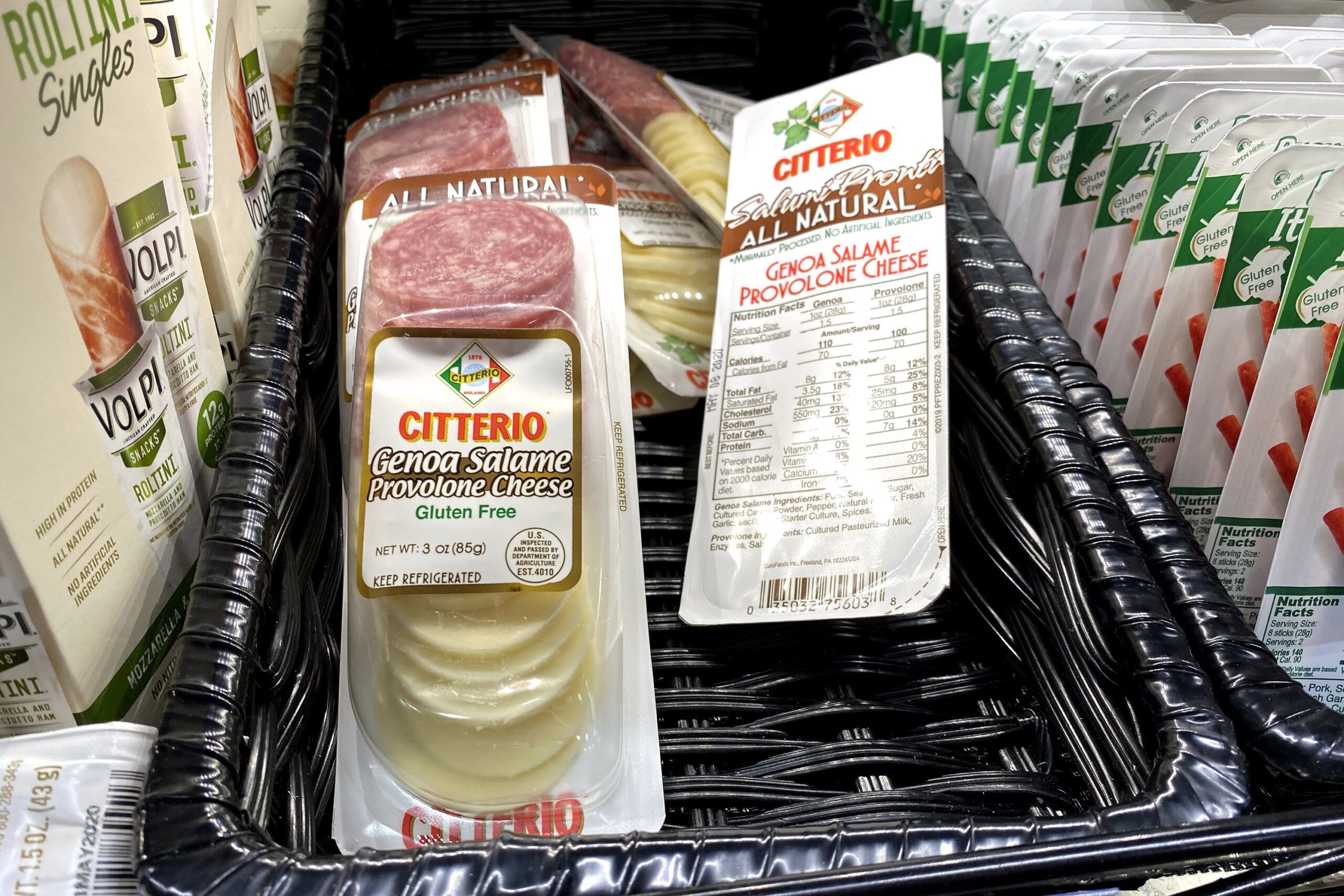 Packages of Citterio Genoa Salame and Provolone Cheese at a Trader Joe's, in a refrigerator in a black basket, other world cheese on both sides