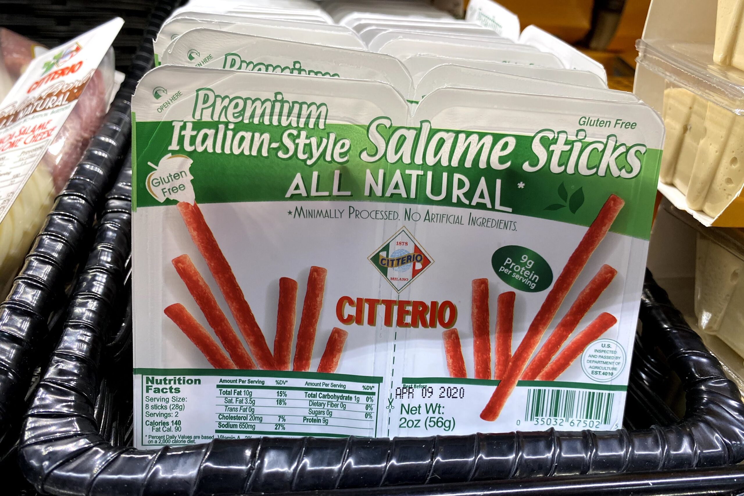 A row of packages of Citterio Salame Sticks at a Trader Joe's, in a refrigerator in a black basket, another world cheese on the left