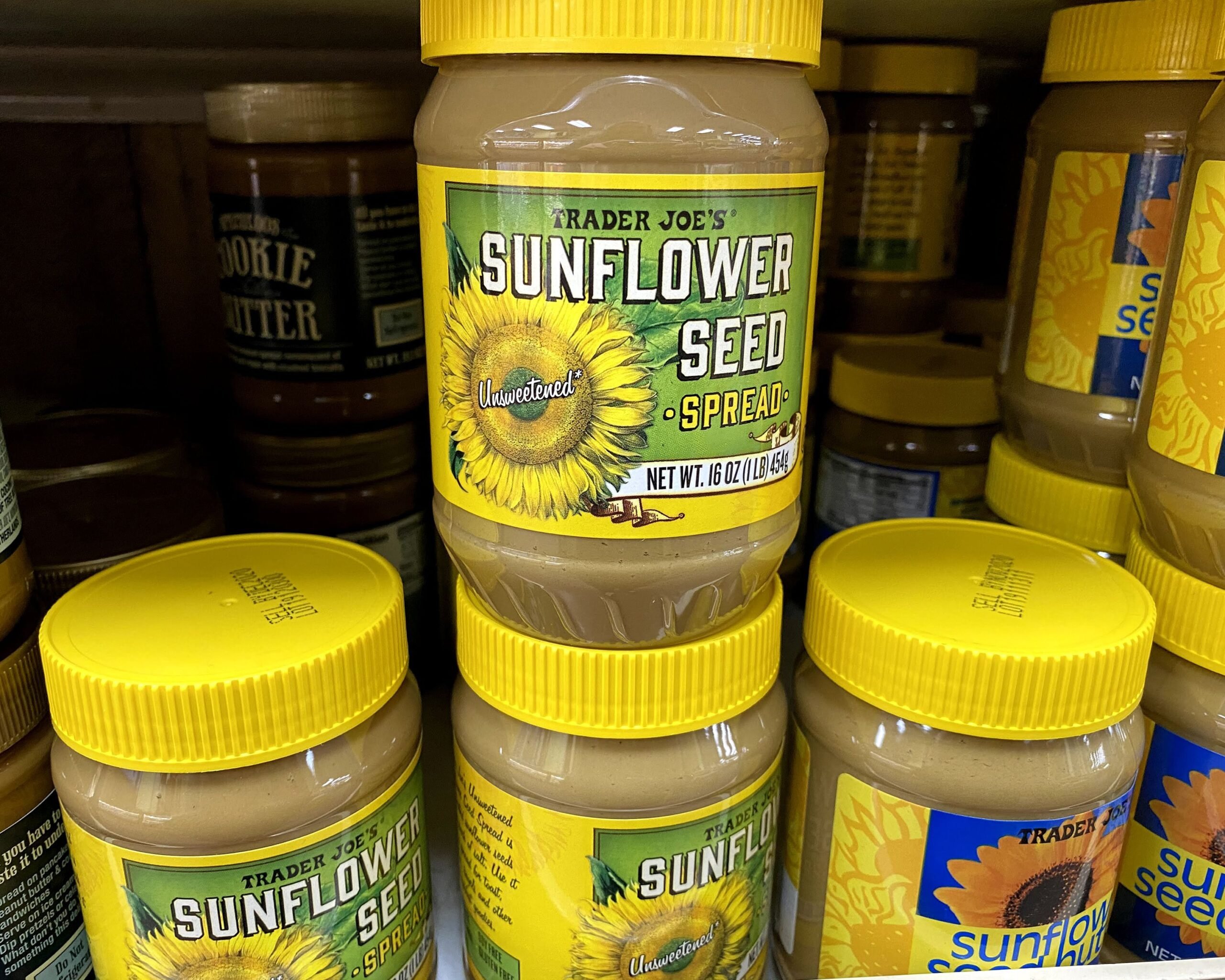Two rows of plastic jars of Trader Joe's Sunflower Seed Spread at a Trader Joe's, on a shelf, butter on both sides