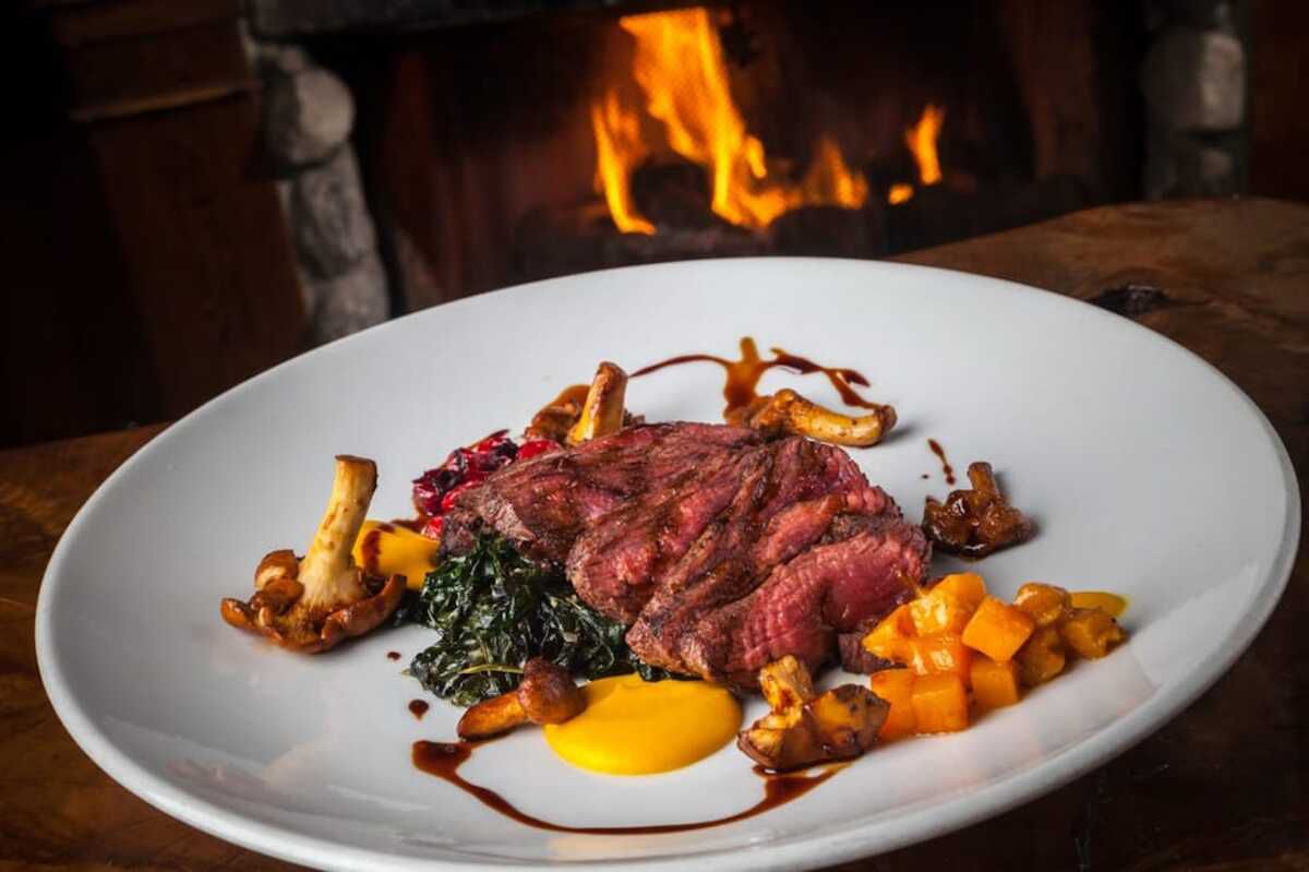 steak with vegetable and sides at Saddle Peak Lodge, Calabasas, California with fireplace in the background
