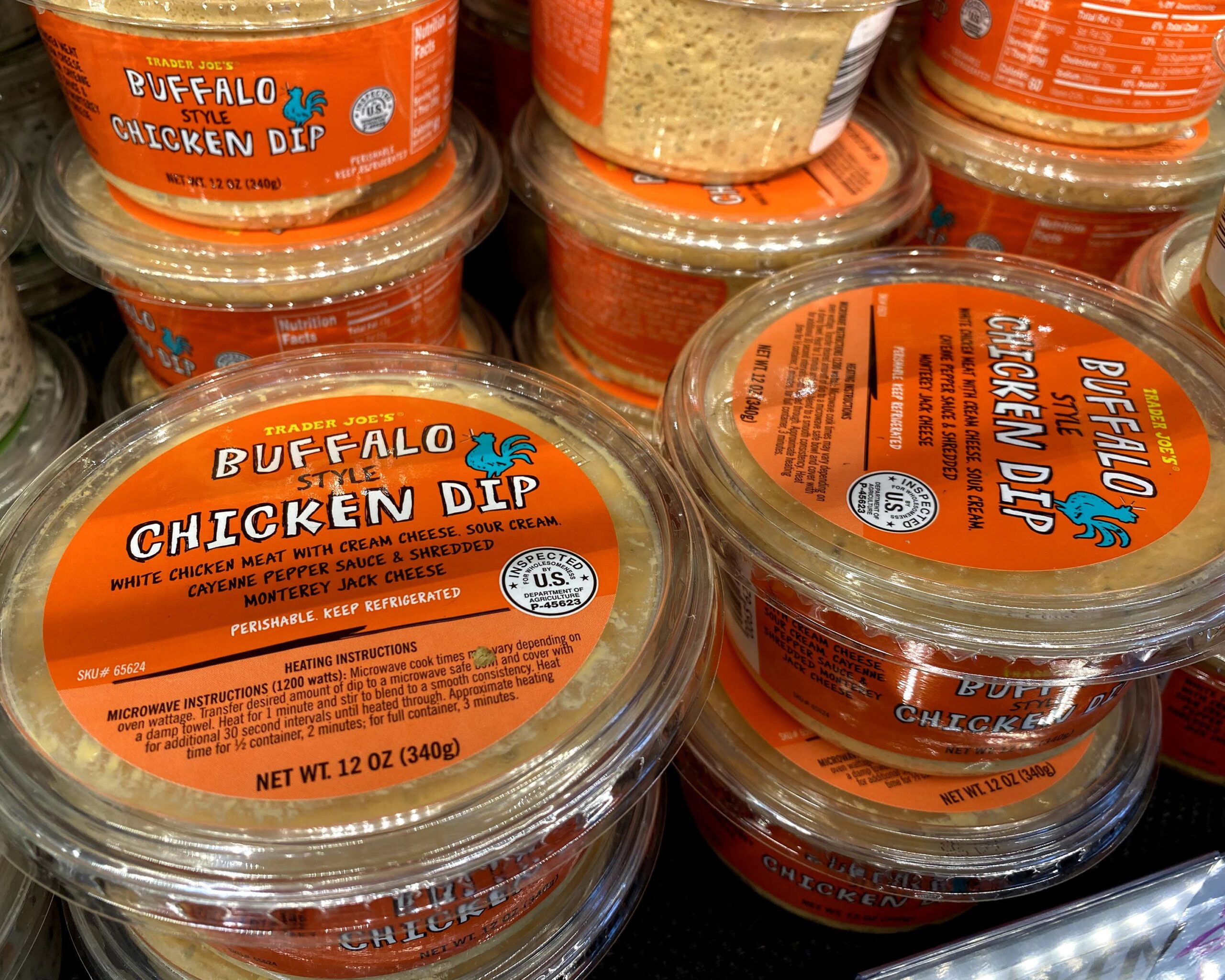 Many stacks of tubs of Trader Joe's Buffalo Style Chicken Dip at a Trader Joe's, in a refrigerator on a shelf