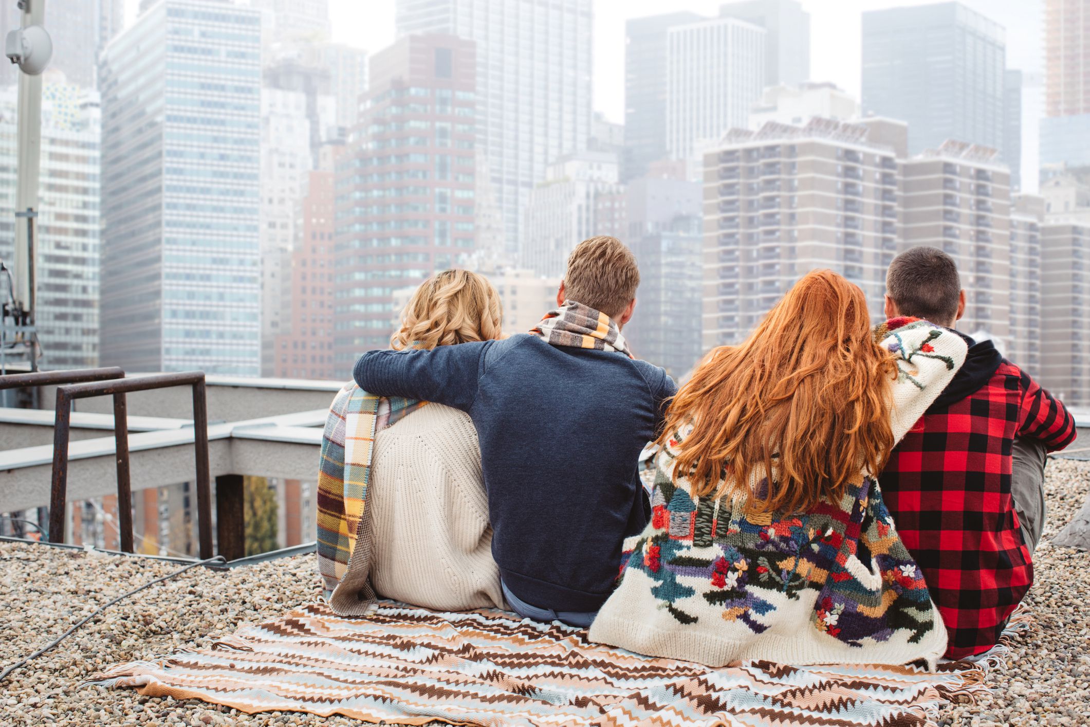 four people sitting on rooftop looking at skyscrapers
