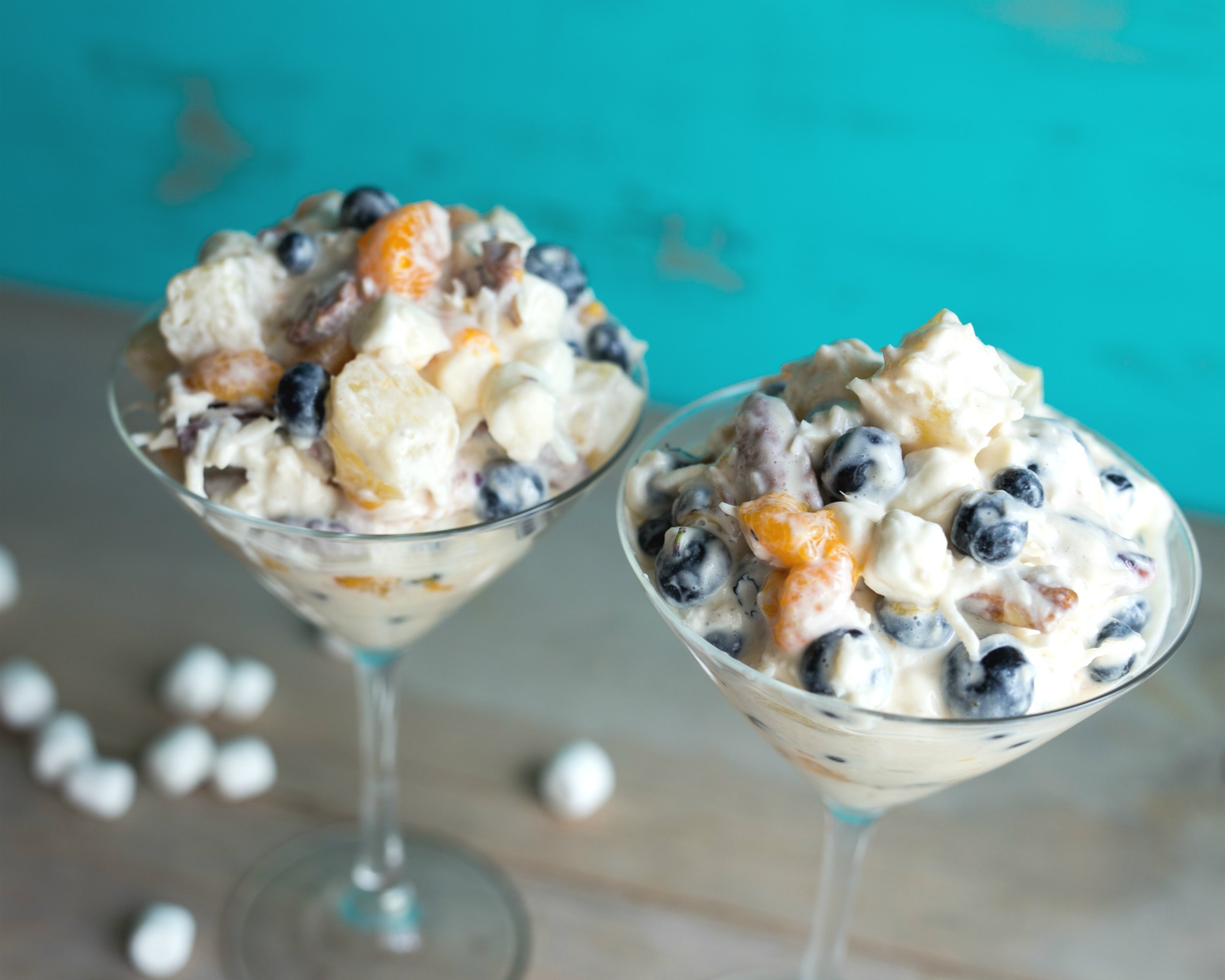 ambrosia fruit salad in two martini glasses against a turquoise background
