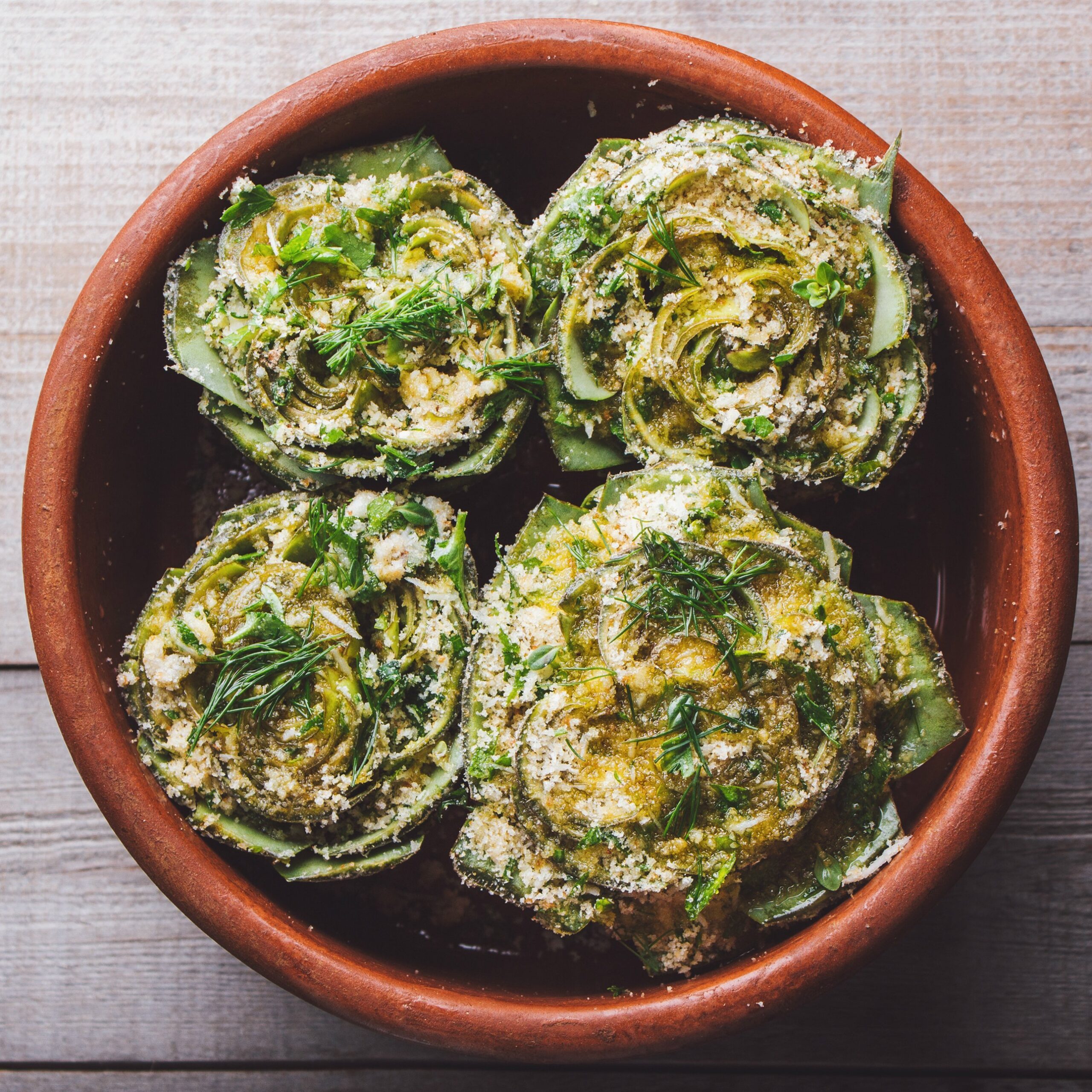 cooked artichokes with parsley and parmesan, served in a clay dish on a wooden table