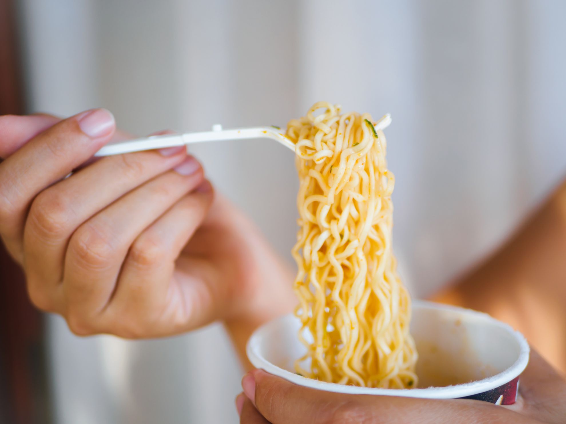 Hand holding fork to eat spicy instant noodles in cup, Sodium diet high risk kidney failure. Healthy eating concept.