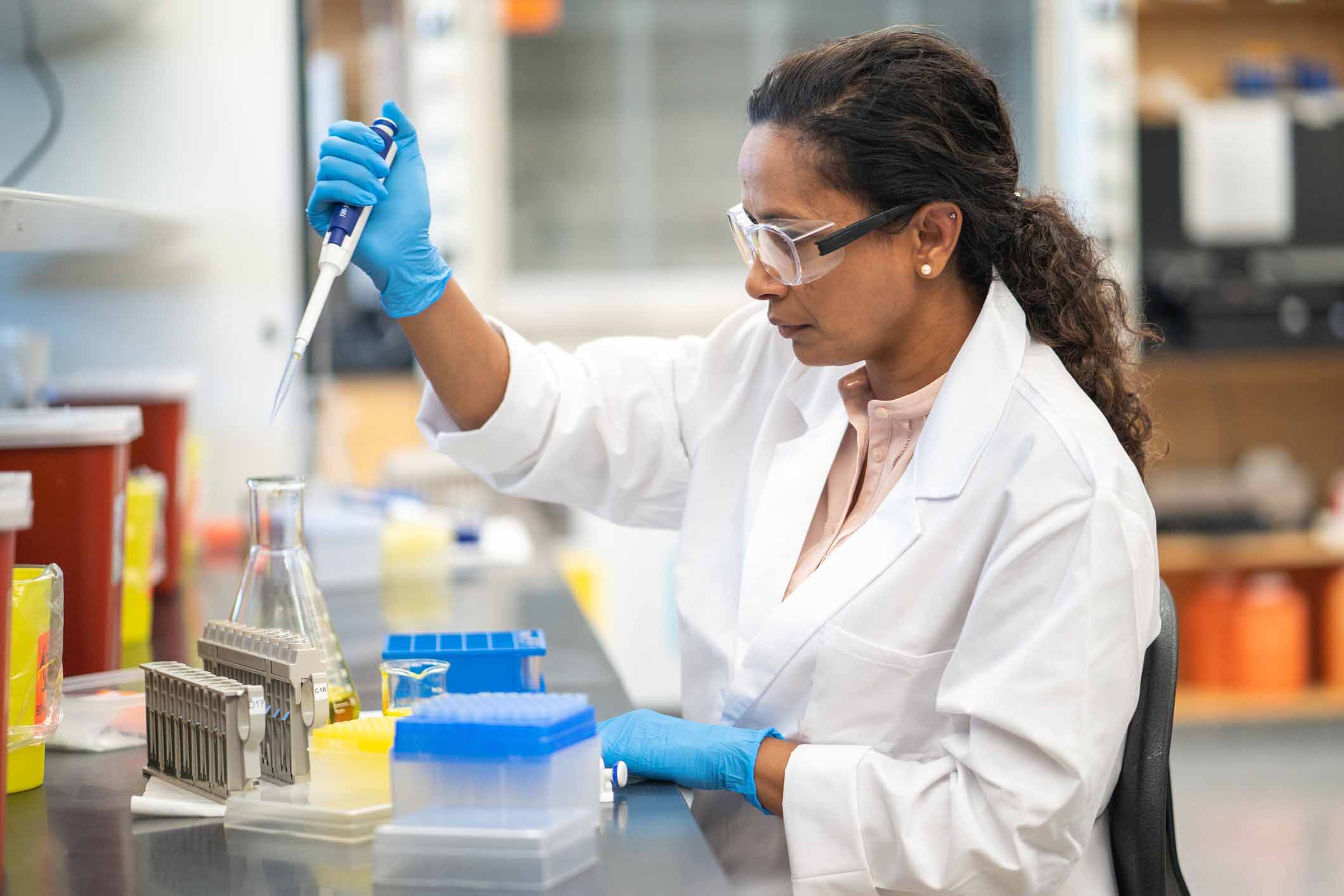 biochemist is working in a laboratory. She is seated at a work station and is using a pipette. The researcher is going to analyze the medical sample.