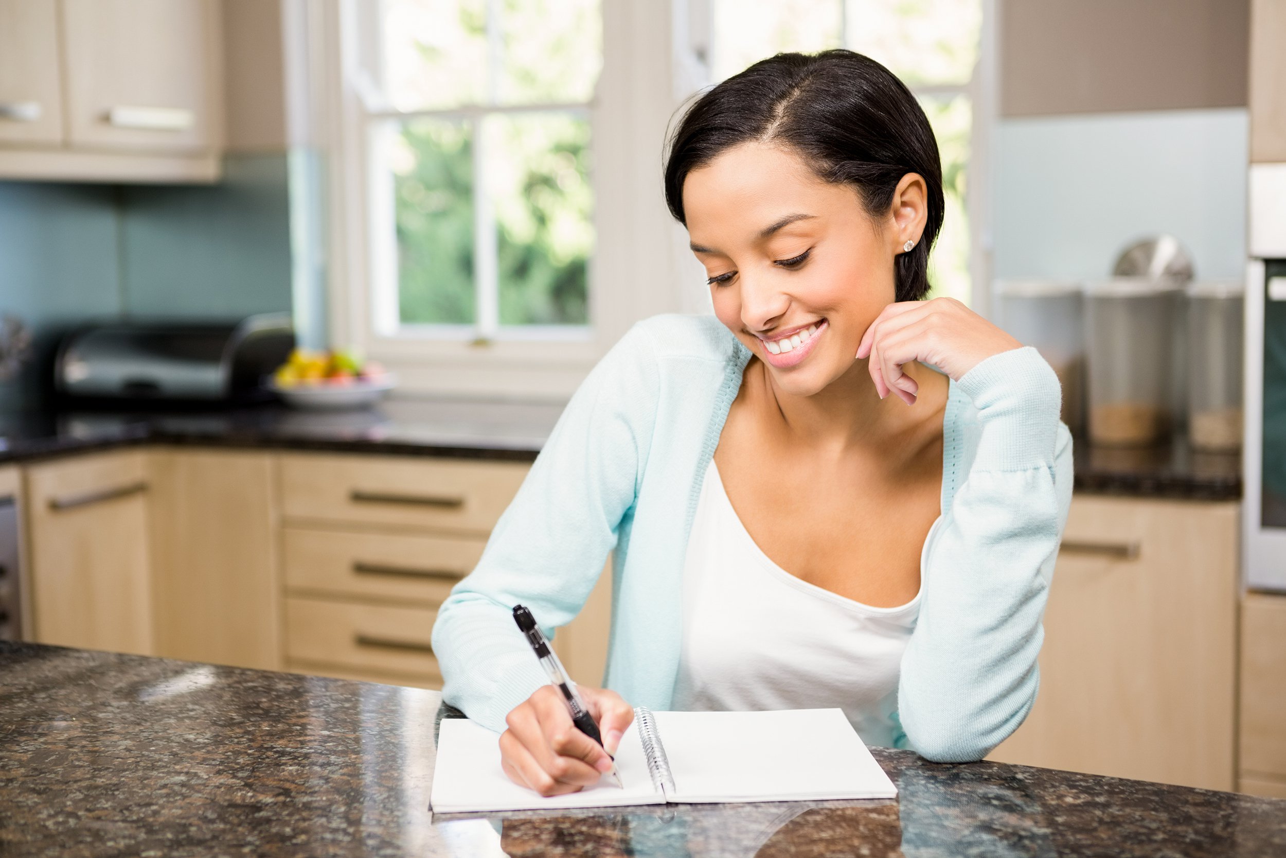 smiling mixed-race woman writing on note pad in kitchen