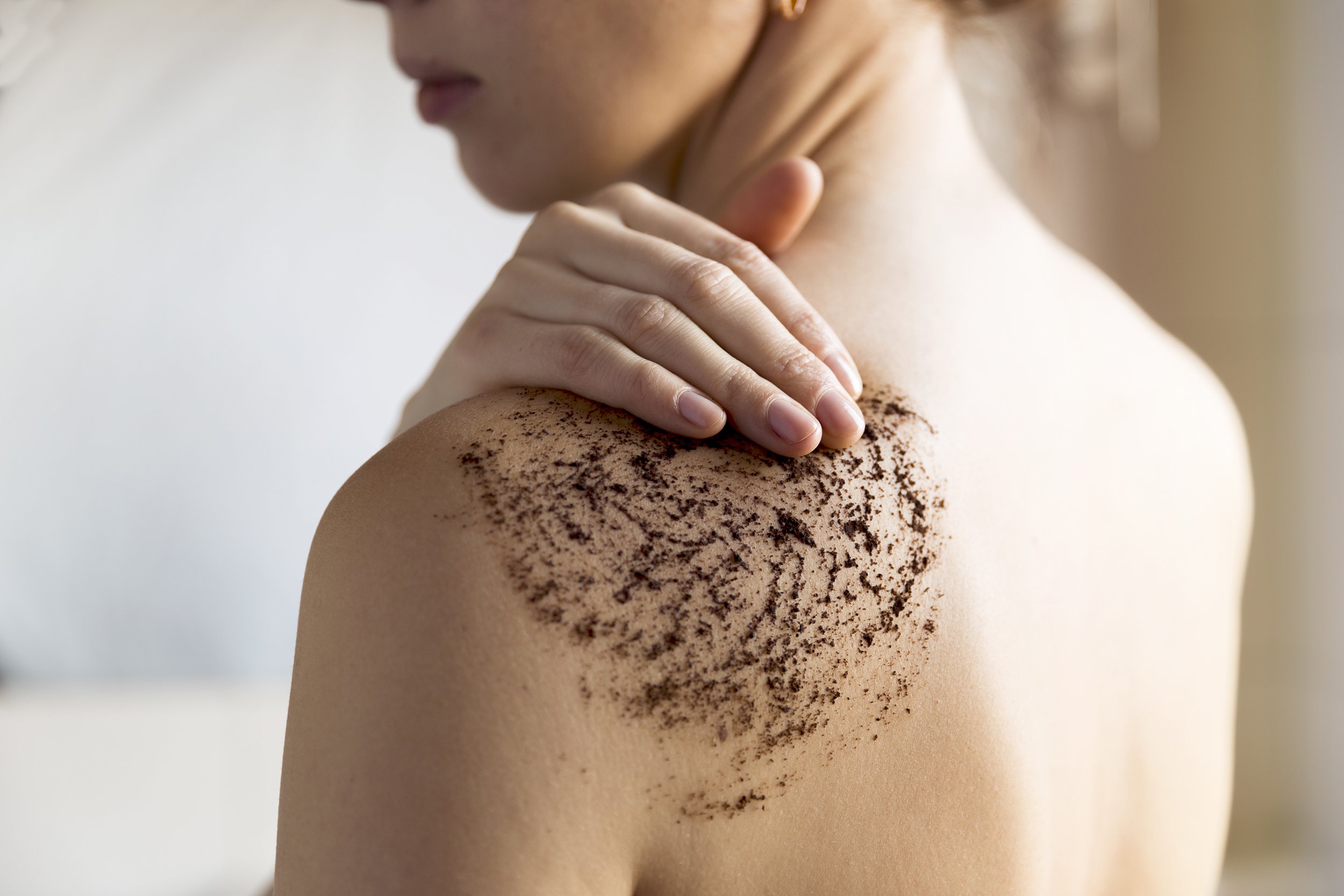 woman cleans skin of the body with coffee scrub in bathroom