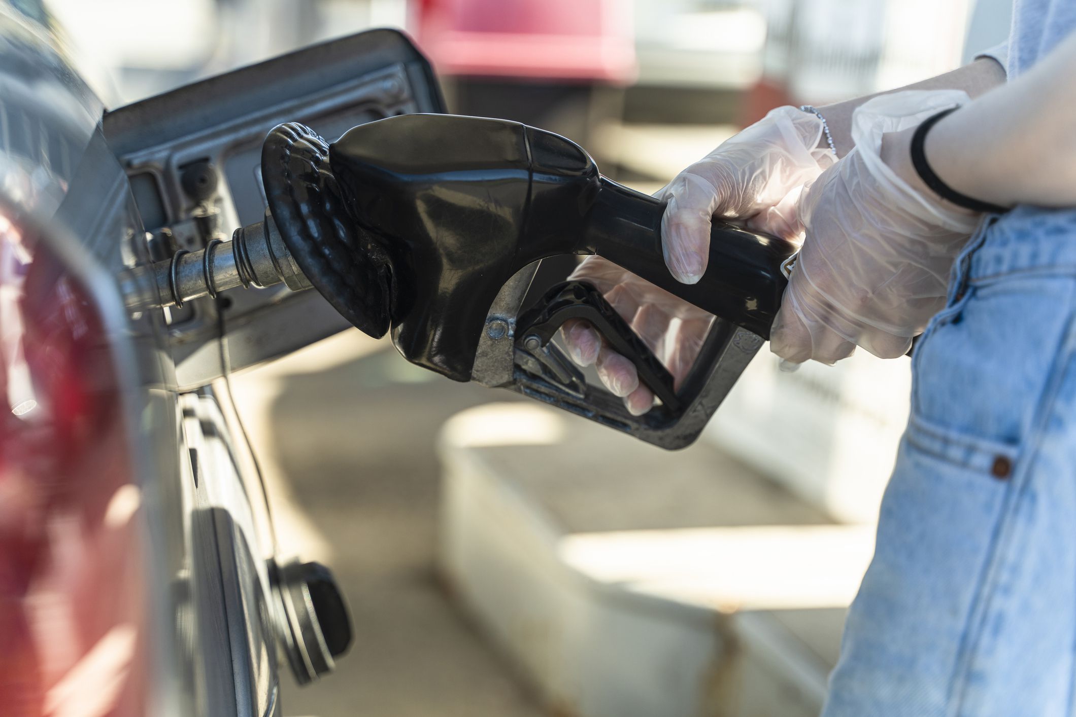 woman refueling a car at the gas station. She wearing protective latex gloved to prevent spreading infection because of COVID-19 coronavirus outbreak