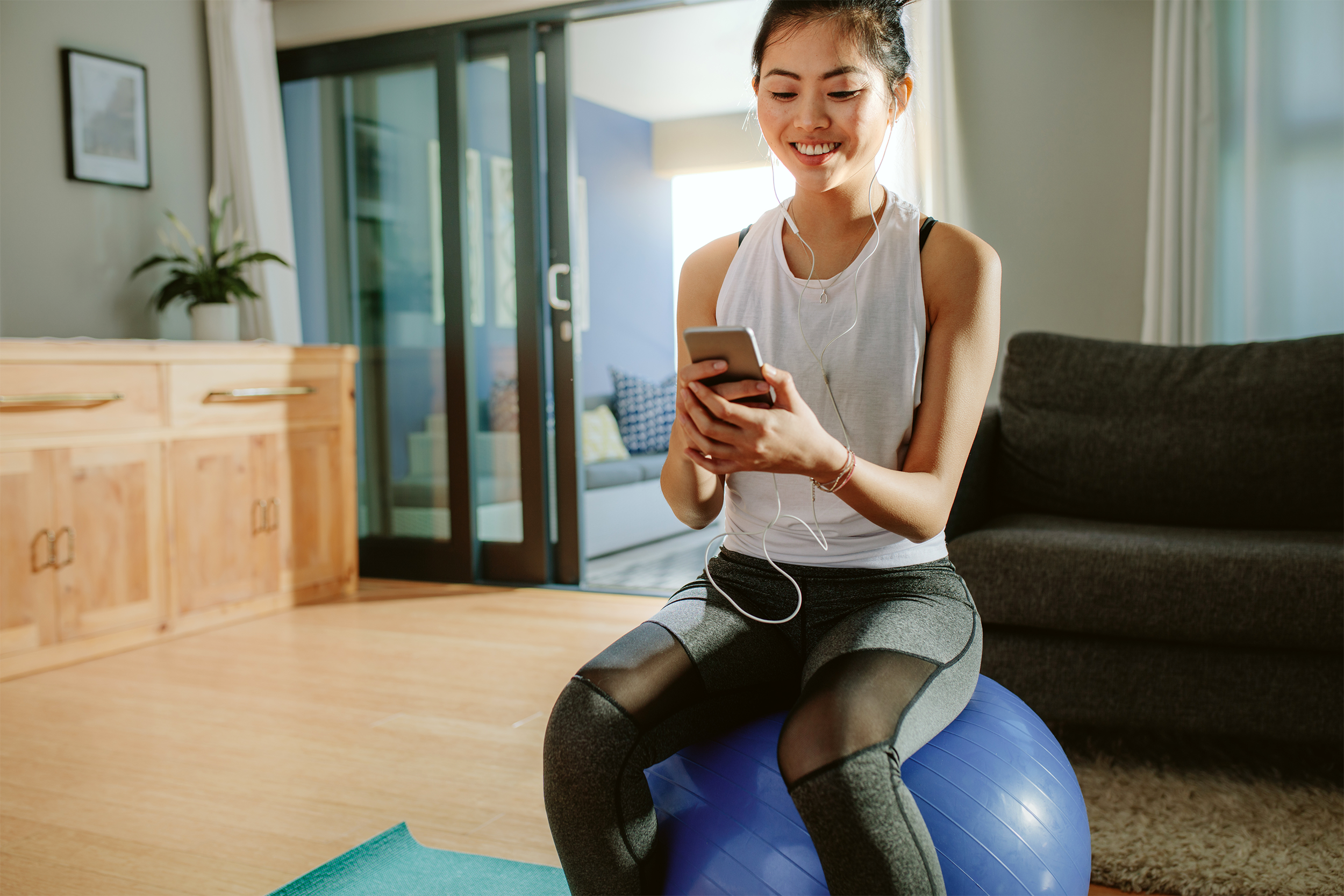 Woman sitting on yoga ball at home holding her phone