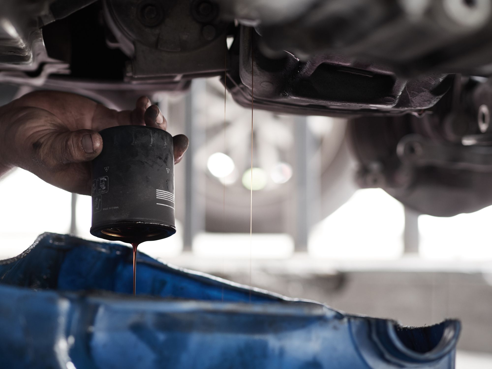 Professional car mechanic changing motor oil under car at the garage