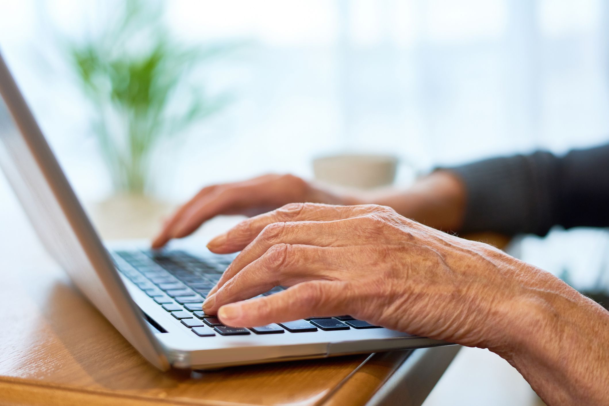 senior hands typing on laptop