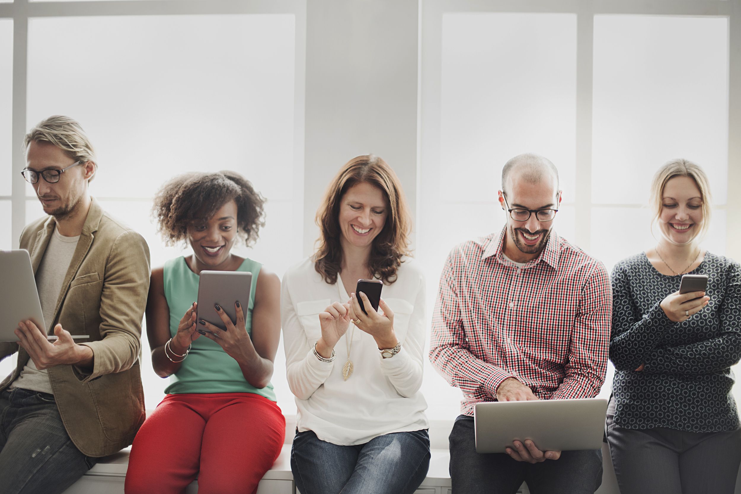 group of people sitting in hallway, all on laptops, tablets and mobiles
