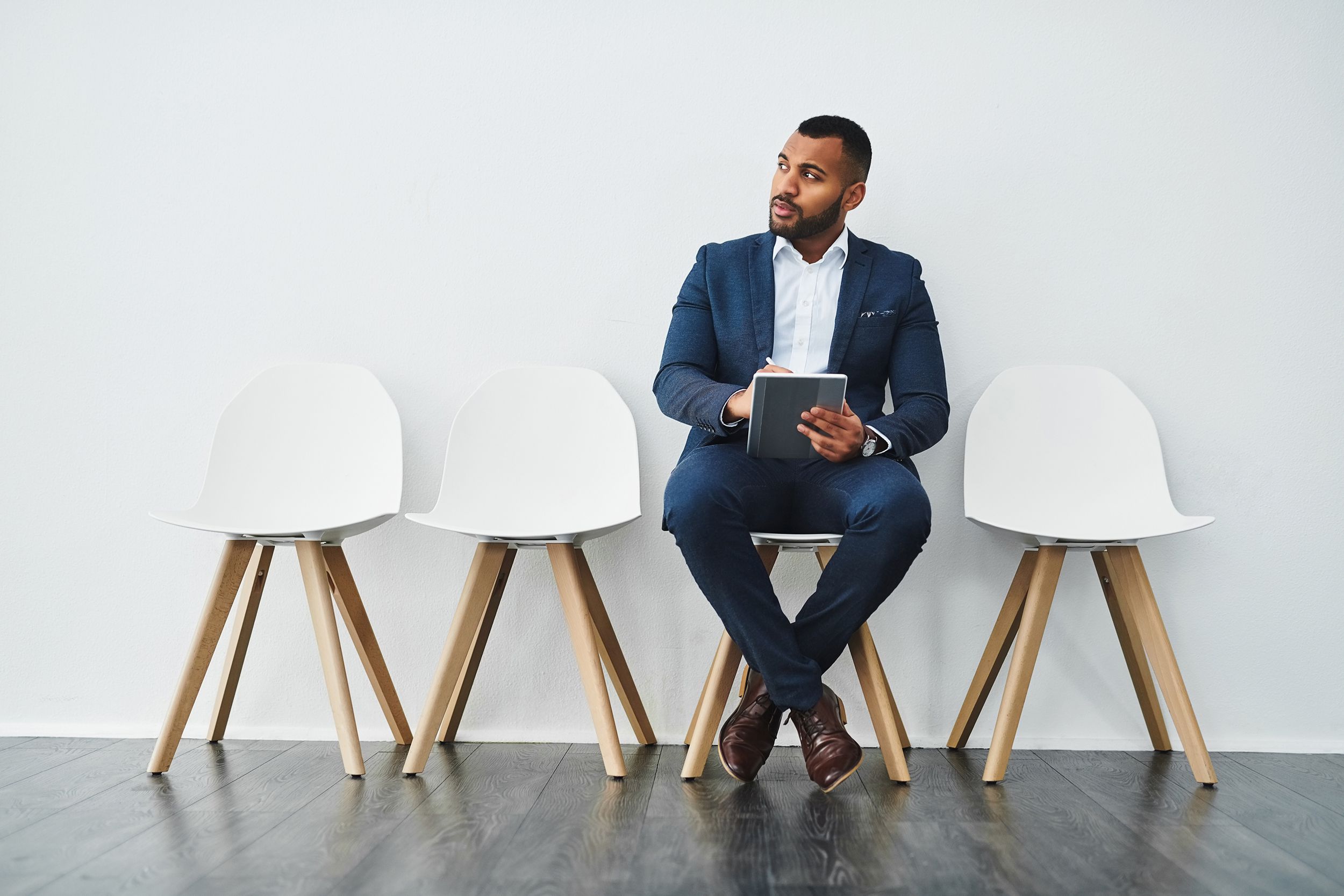 man waiting for job interview, sitting in chair, with three other empty chairs