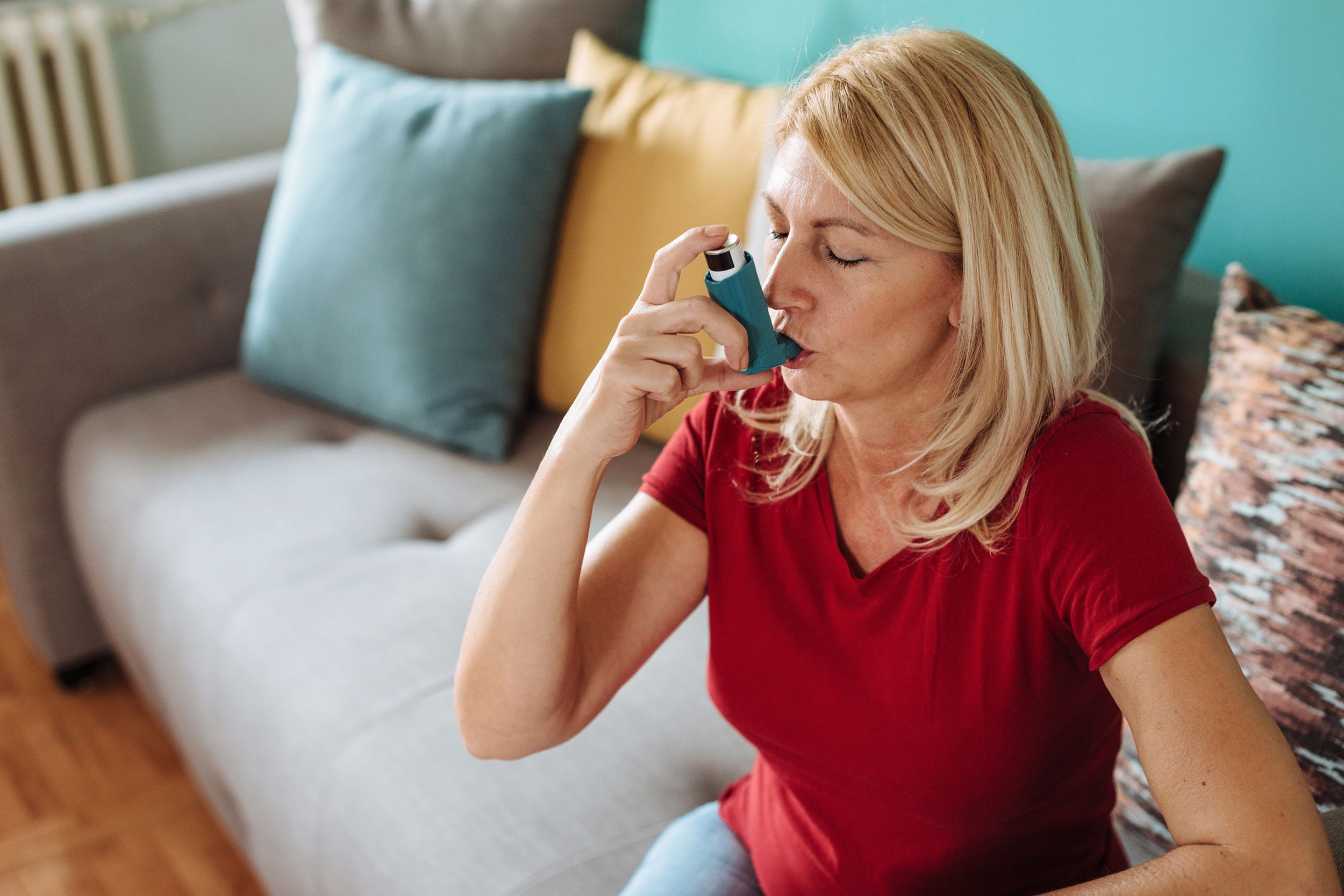 woman using inhaler for asthma while sitting on couch