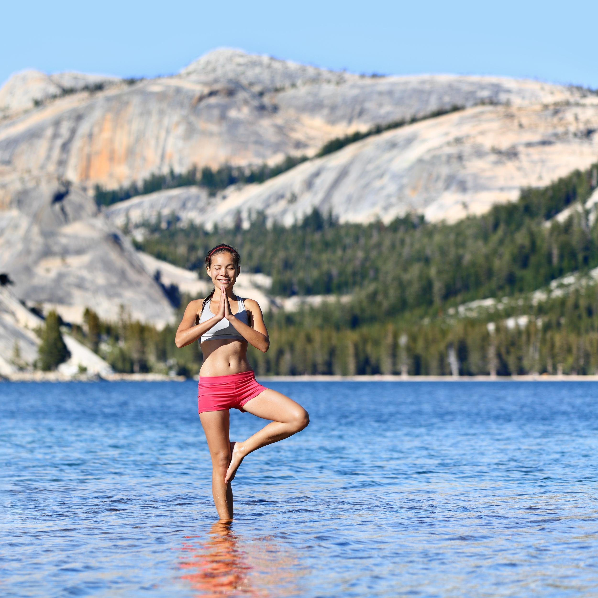 woman doing tree pose outside in the lake and mountains