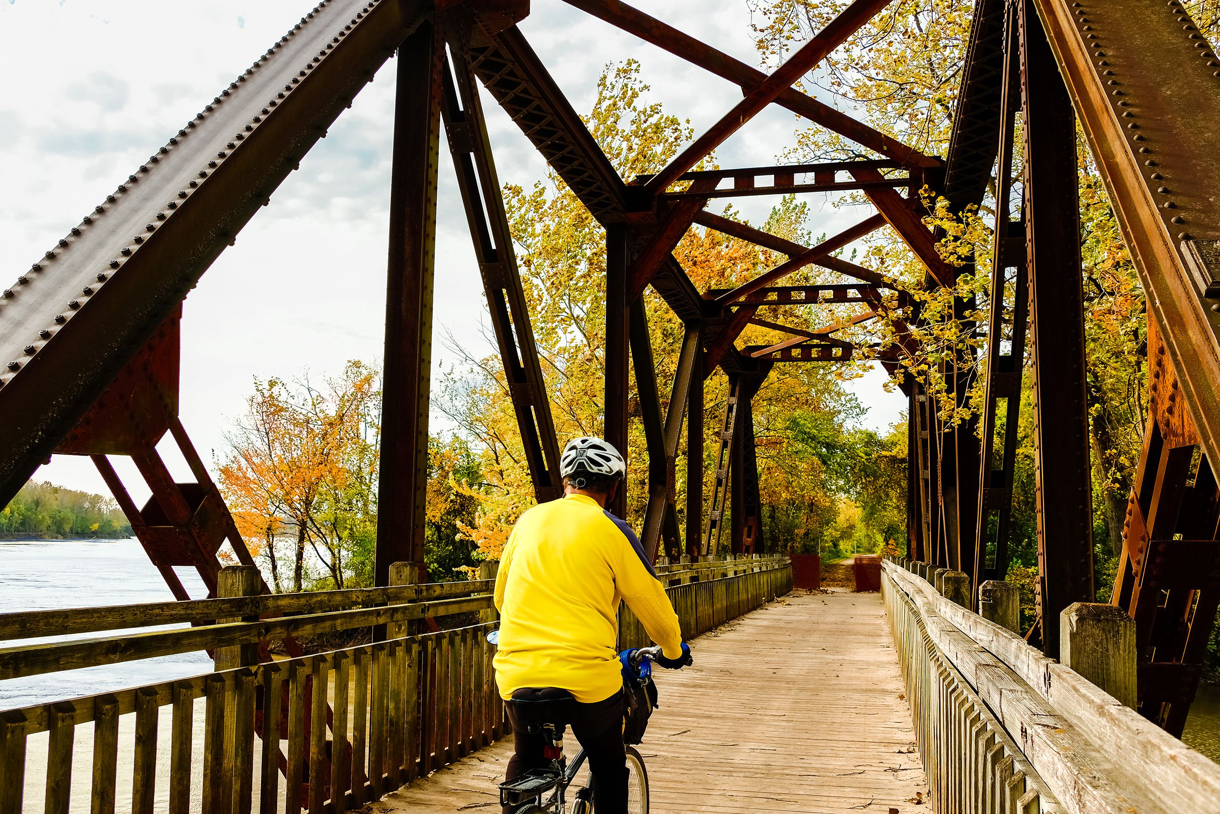 senior male bicyclist in yellow jersey riding old railroad bridge converted into recreation trail