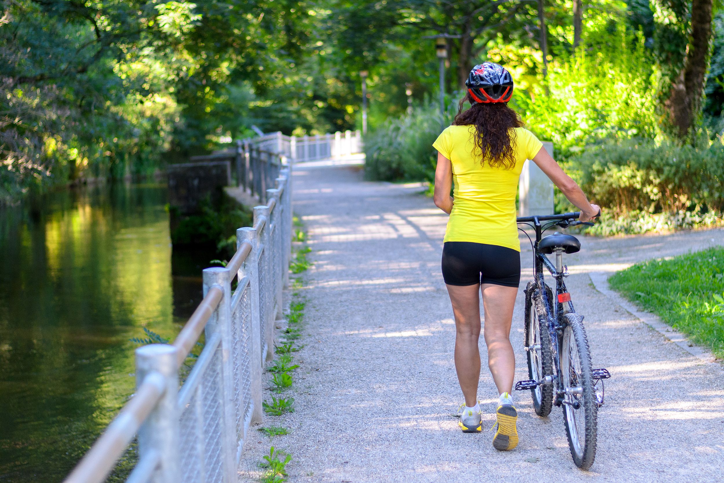 woman wheeling her bicycle along a road alongside a canal