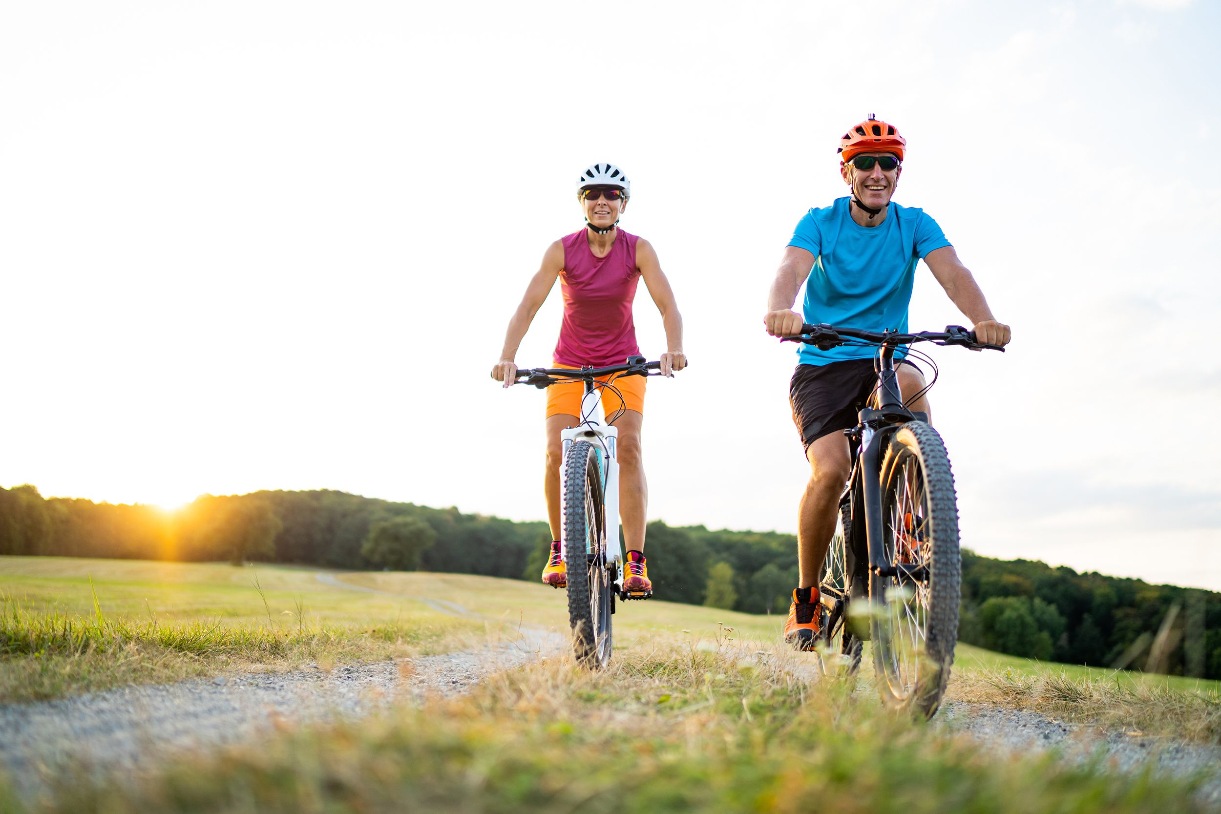 happy smiling woman and man couple friends in their fourties cycling with their electric mountain bicycles on gravel path through grassland