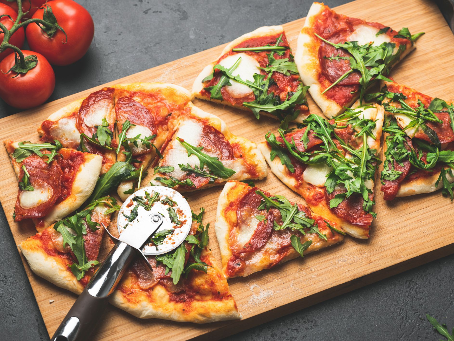 Pizza or flatbread with arugula, salami, cheese sliced ​​on wooden cutting pizza board