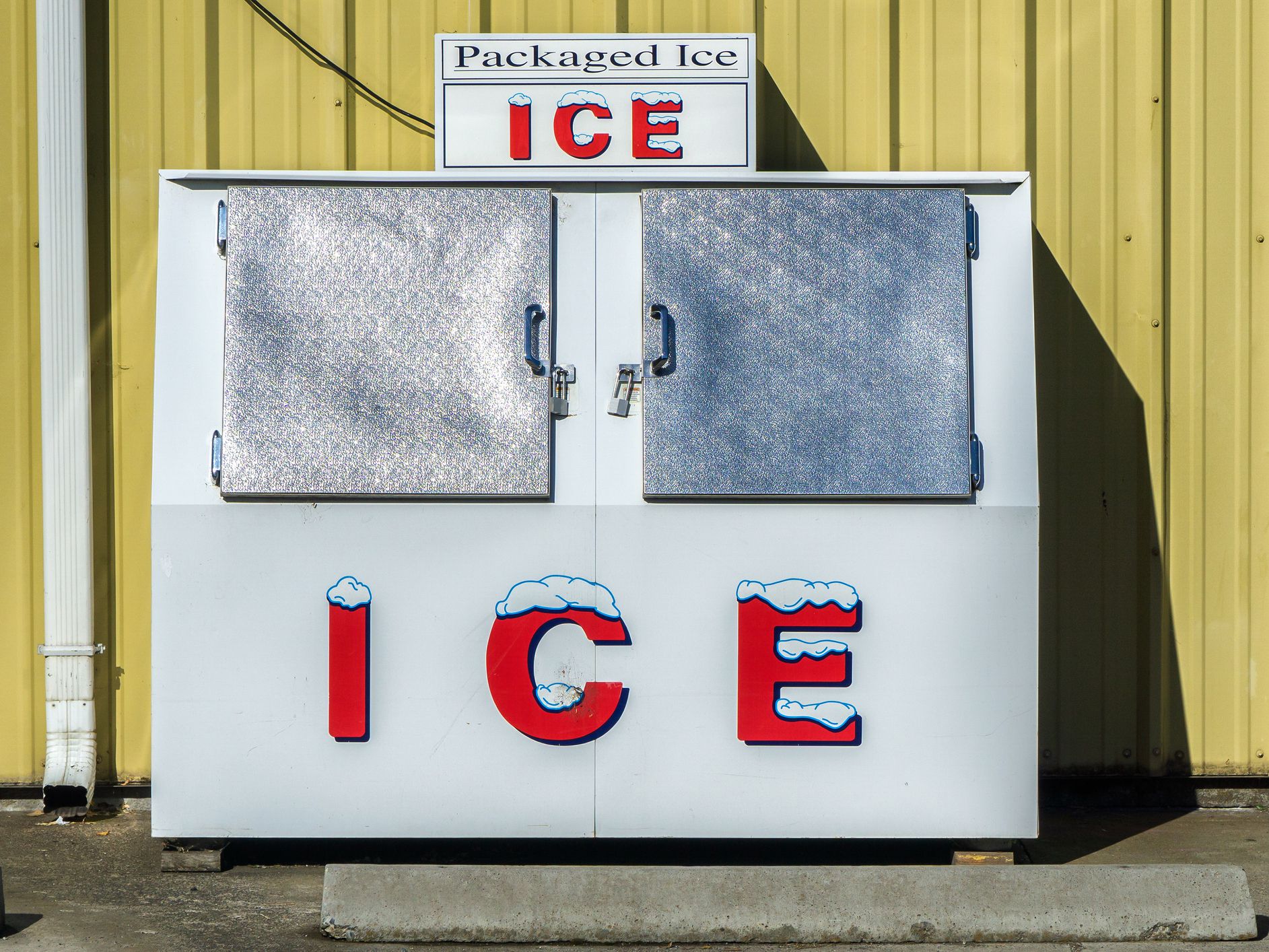 Packaged Ice freezer machine against a yellow wall during a hot and sunny day of summer outside a grocery store, Oregon, USA.