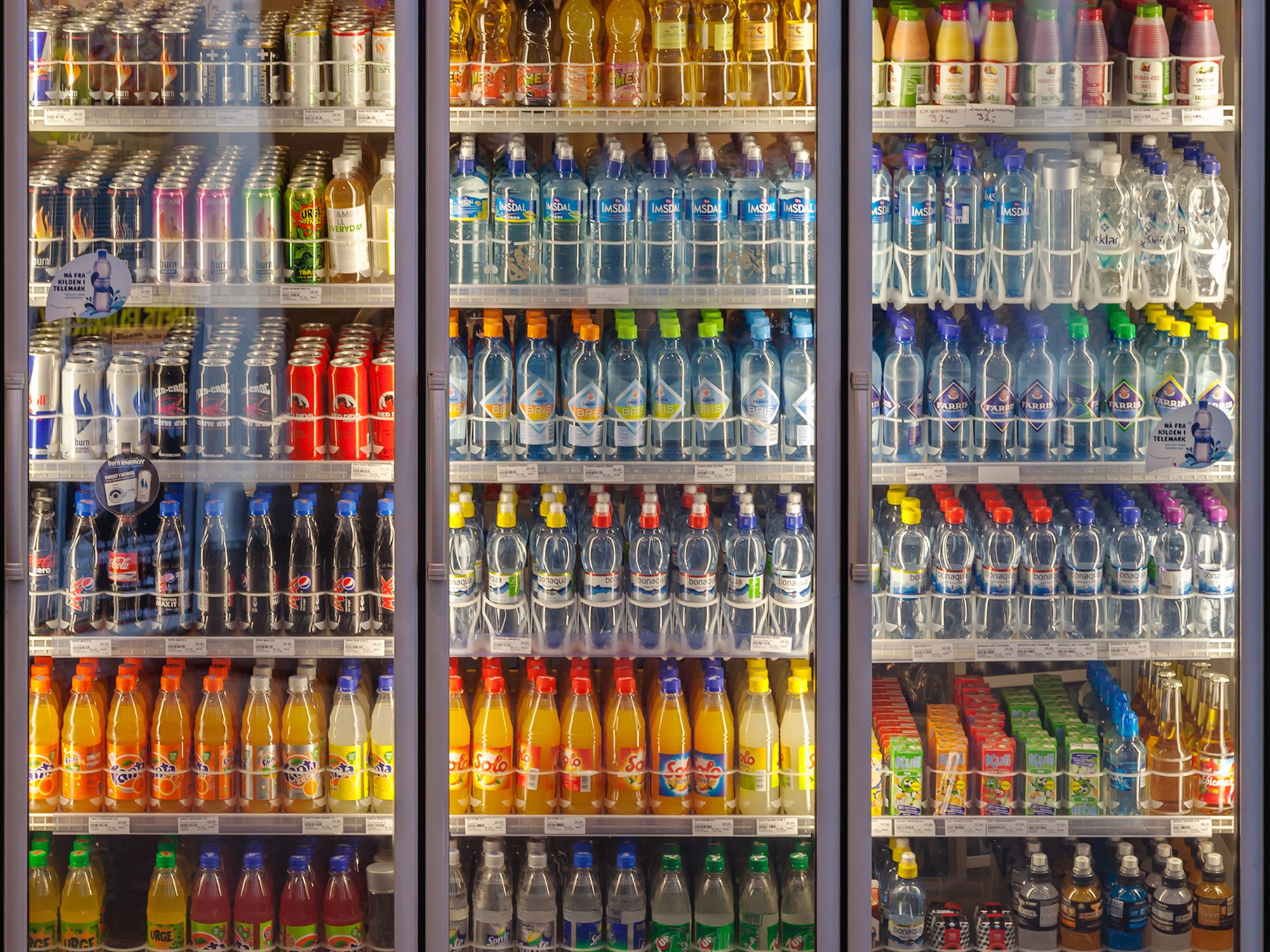 Illuminated three doors vending machine / chiller cabinet, cooling shelves with a diverse range of soft drinks in a shop on the main train stationIn Oslo, Norway