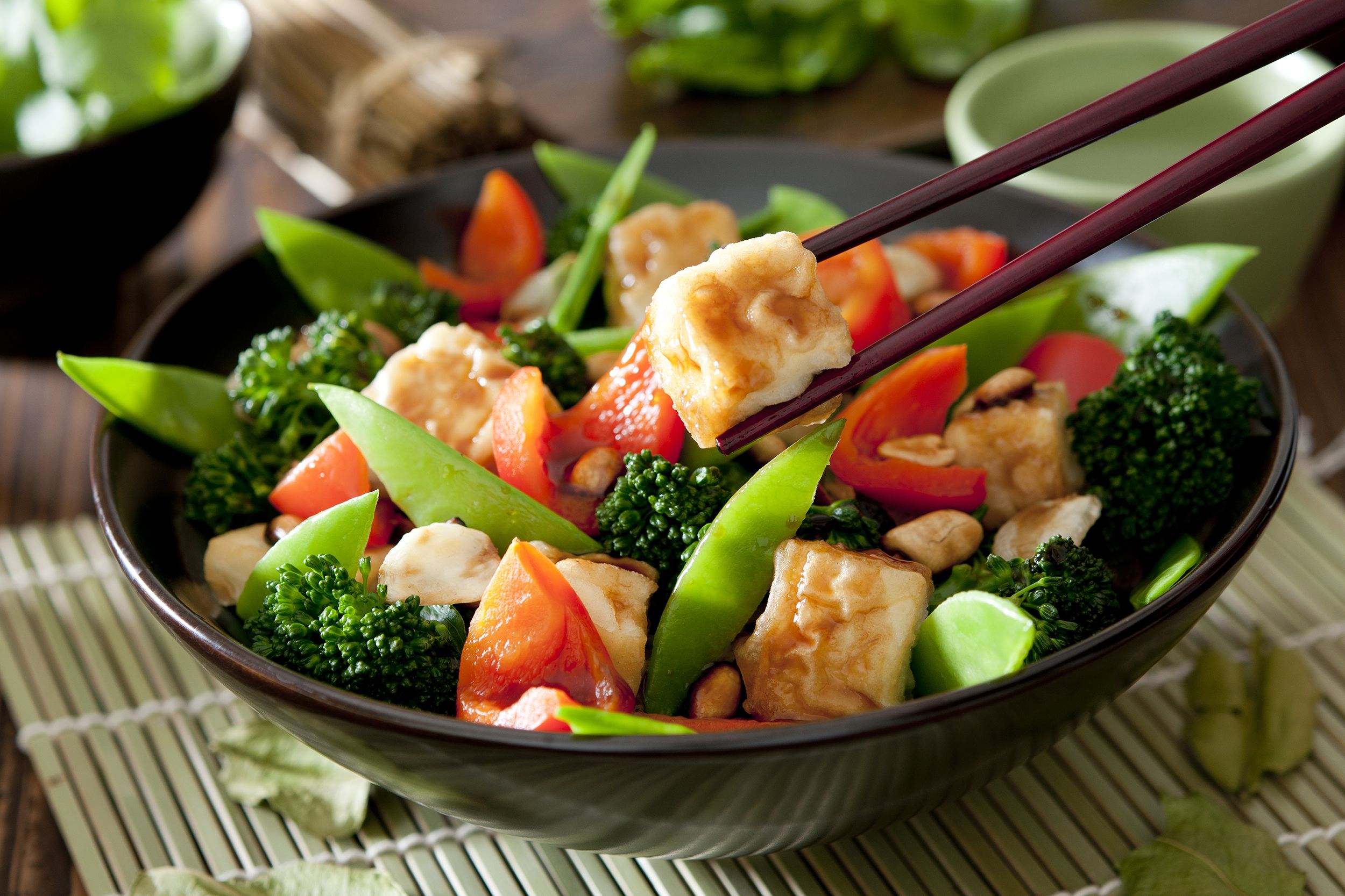 Tofu Stir-Fry in black bowl with chopsticks holding a piece of tofu