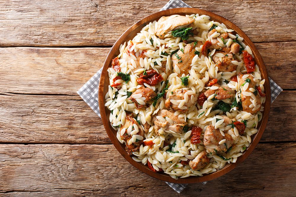Italian pasta orzo with grilled chicken, dried tomatoes, spinach and cheese close-up on the table. horizontal top view from above