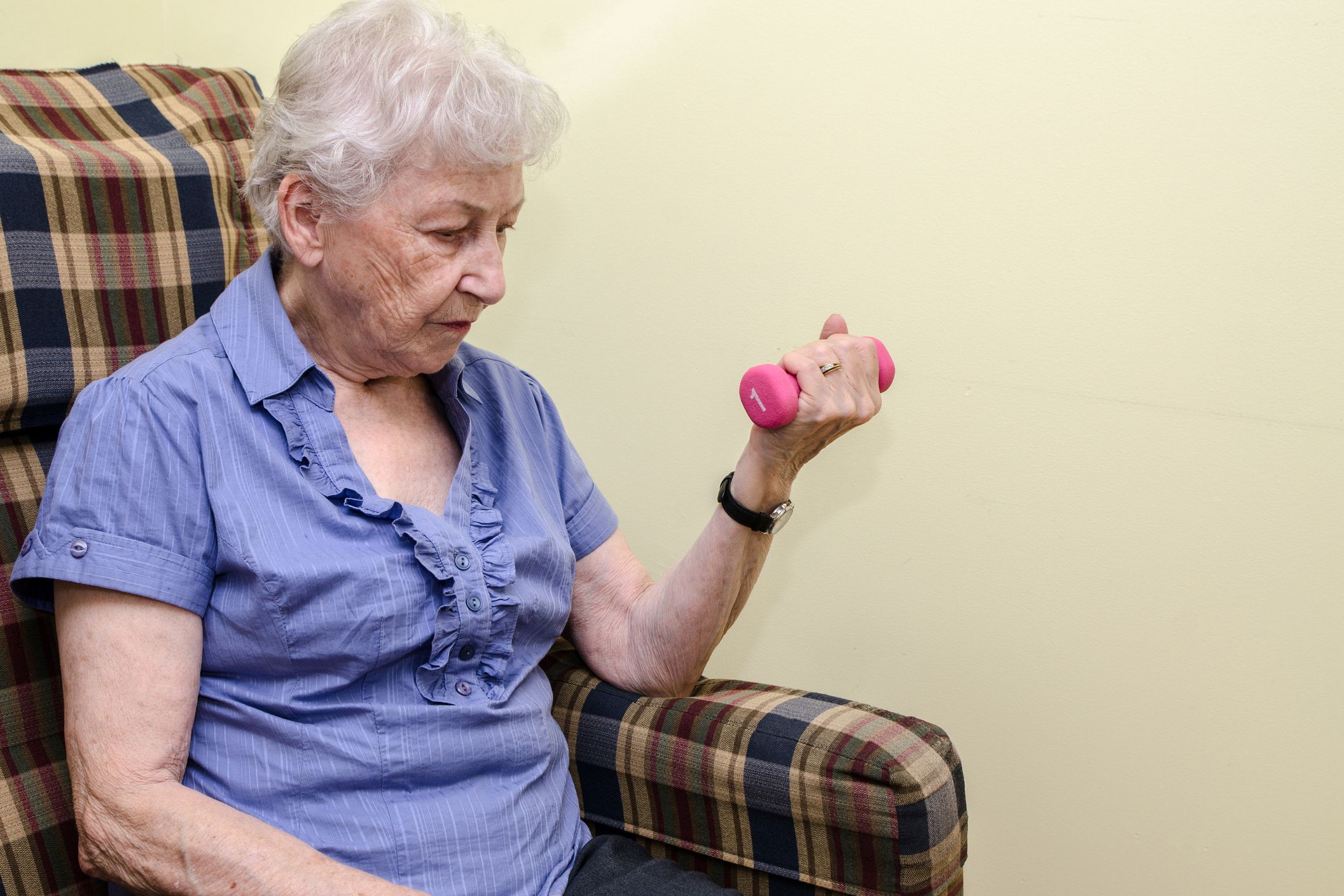 senior woman lifting small hand weight, sitting in chair