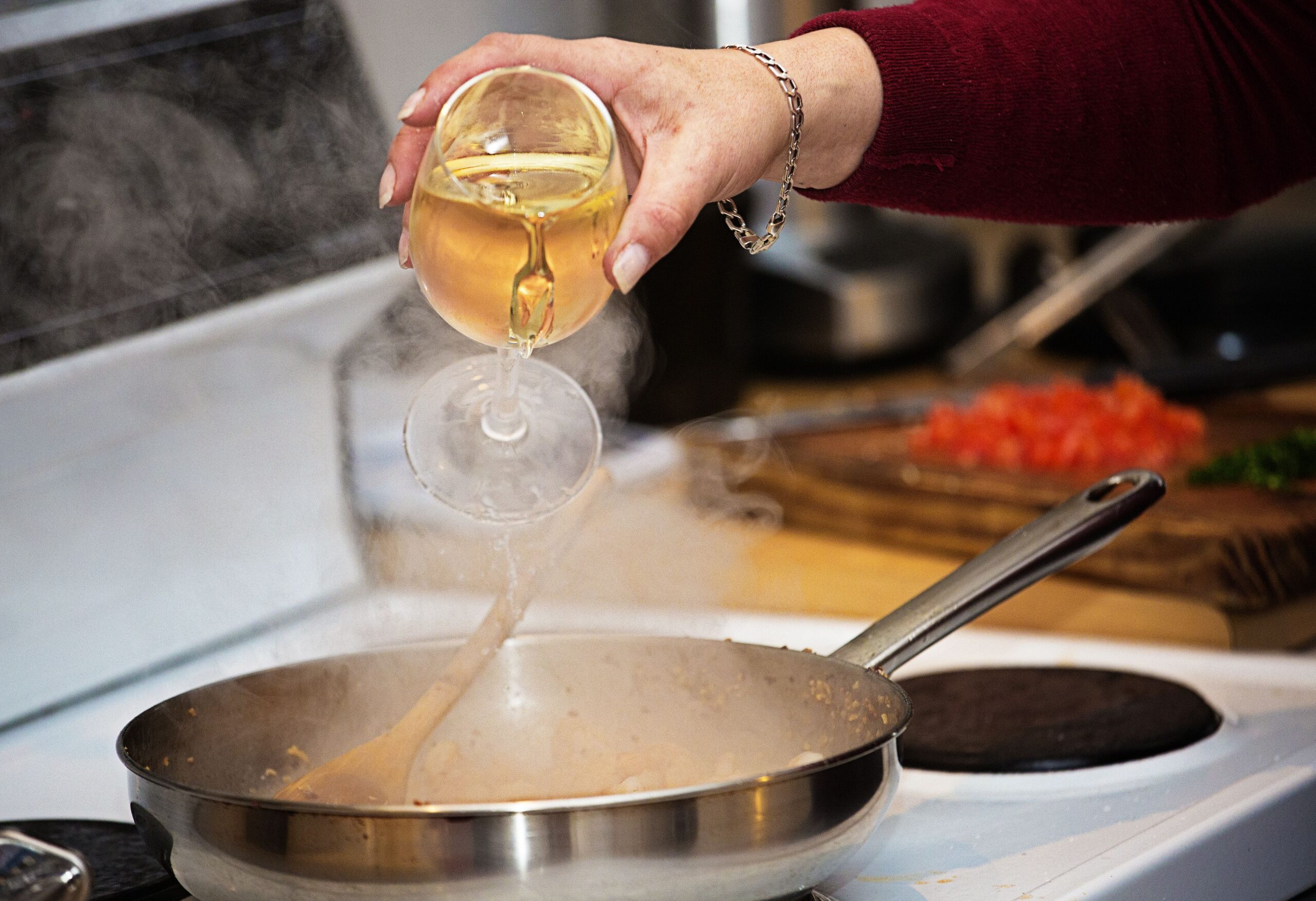 woman pouring white wine into a pan while cooking