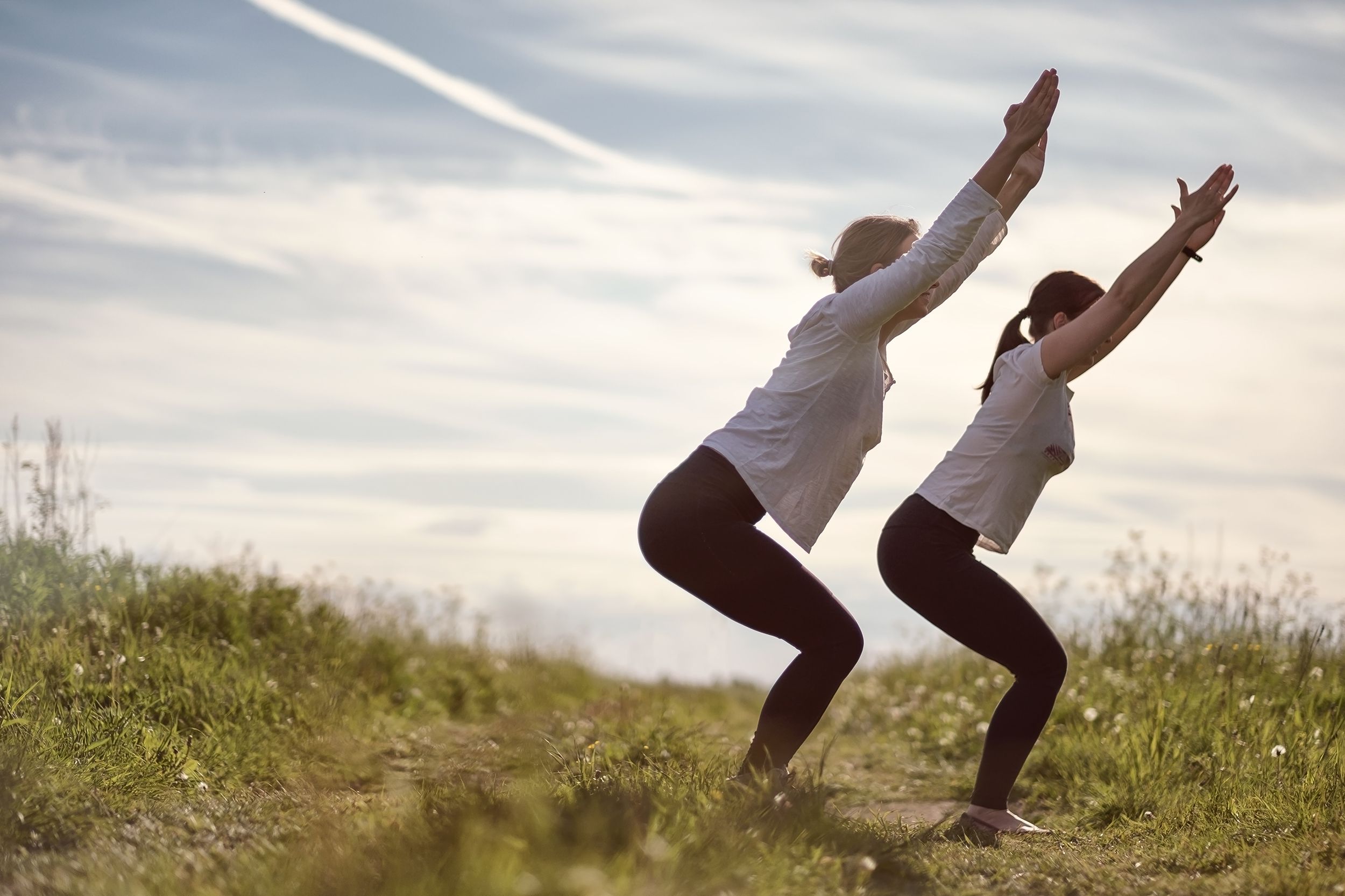 two women doing chair pose outside