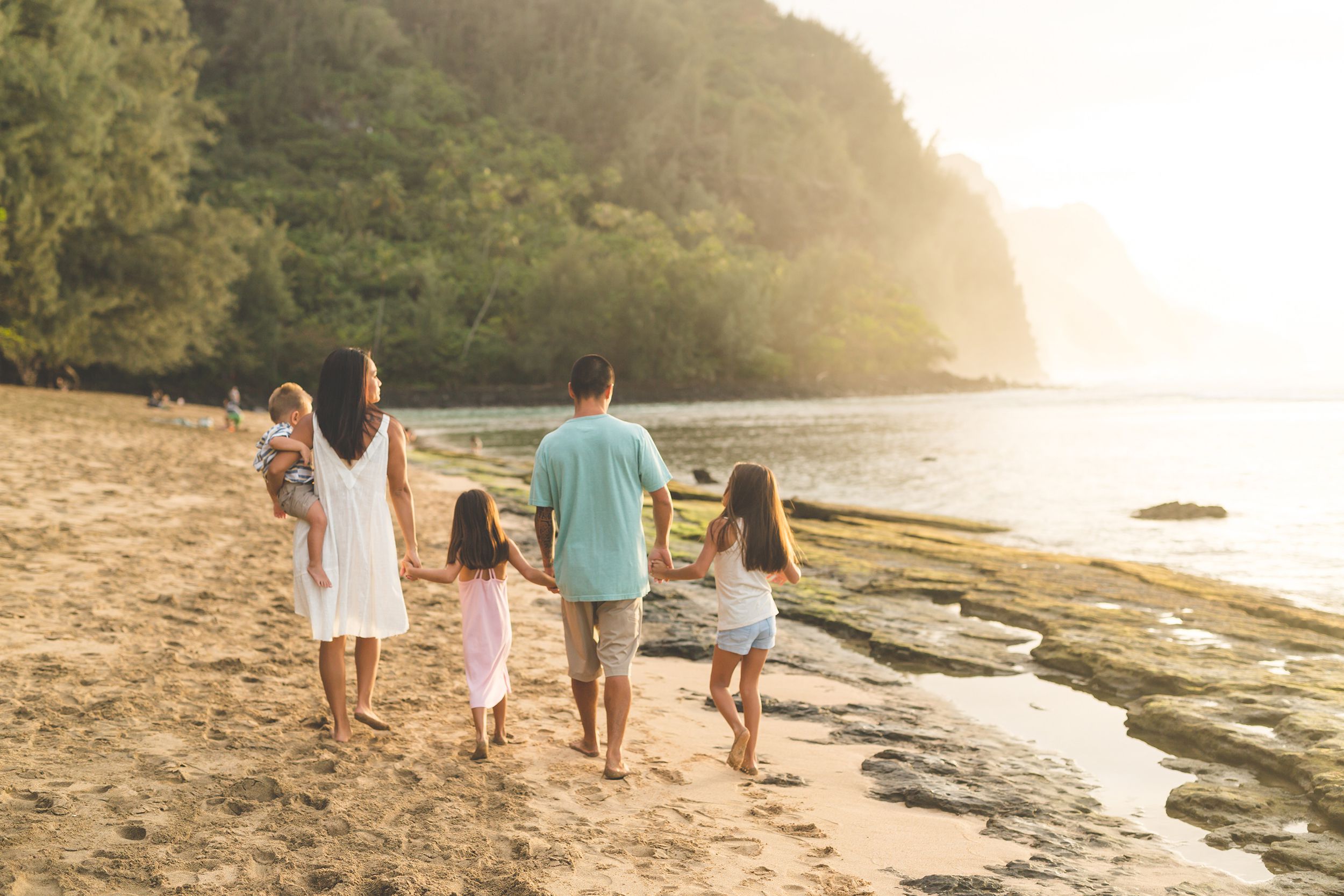 mom and dad walk along the beach with their three children