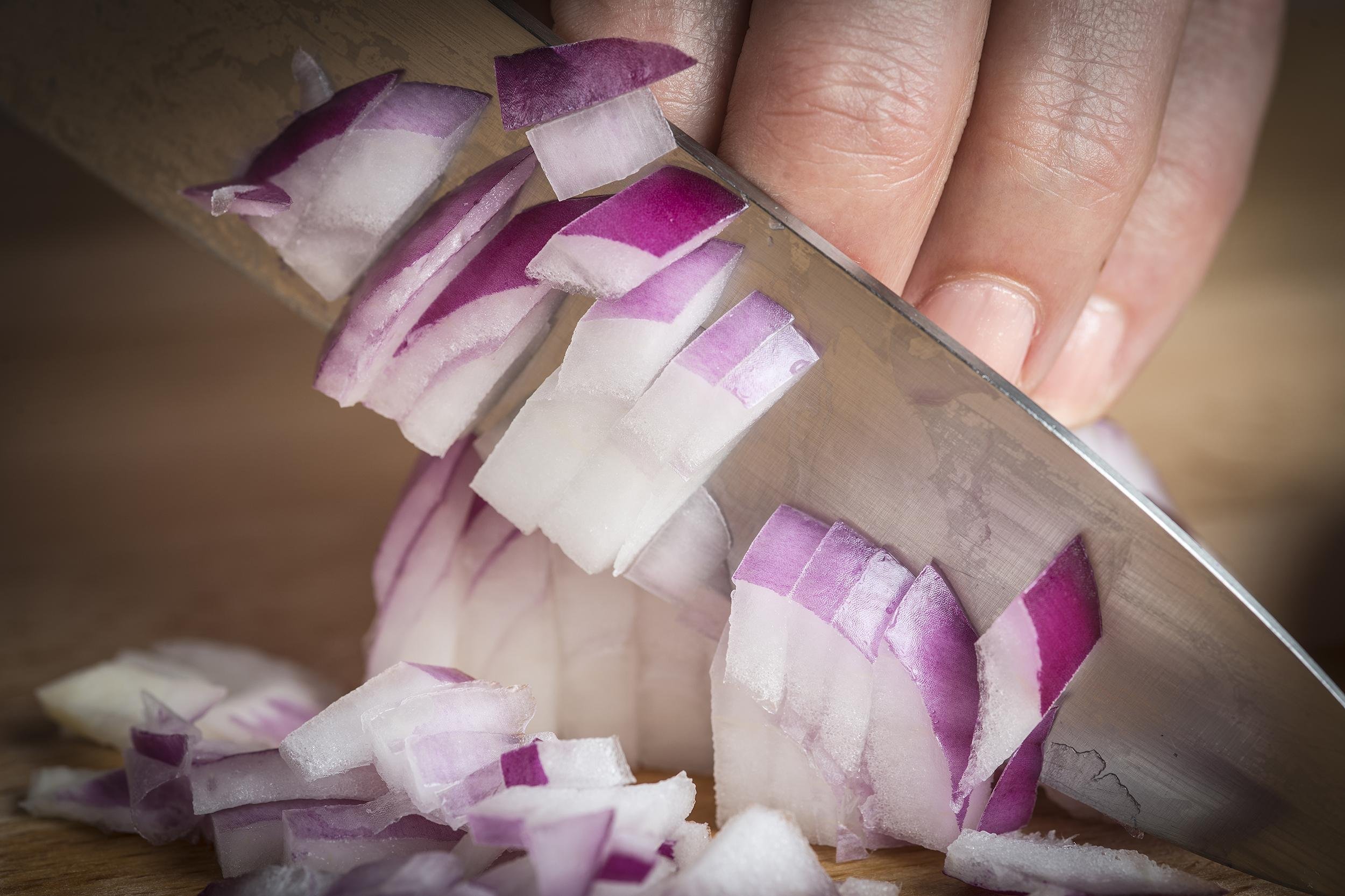 chef chopping a red onion with a knife on the cutting board