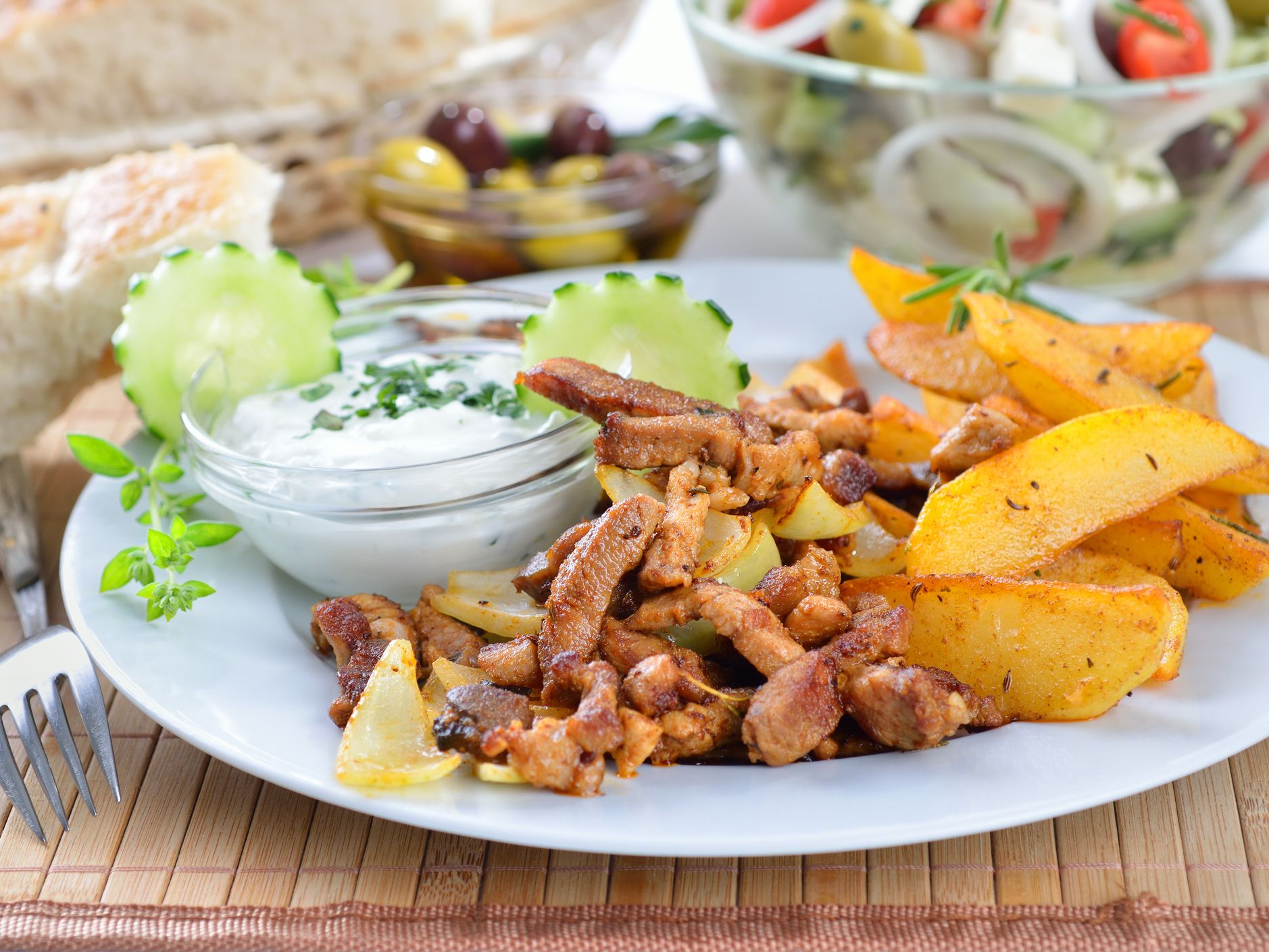Greek pork gyros on a white plate, served with tzatziki and fried potatoes, pitabread, salad and olives