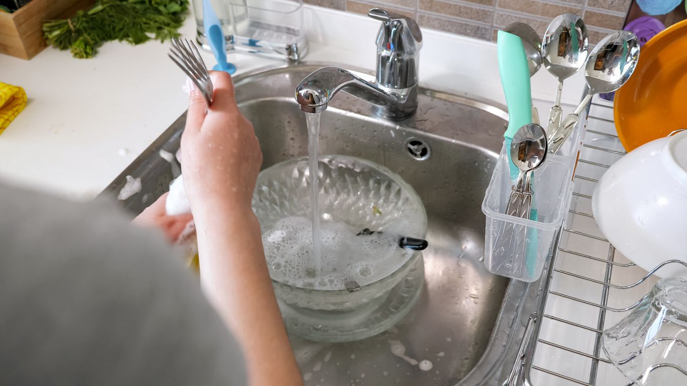 washing cutlery forks by hands soaping sponge with detergents in the kitchen at home in the metal sink, view from the back