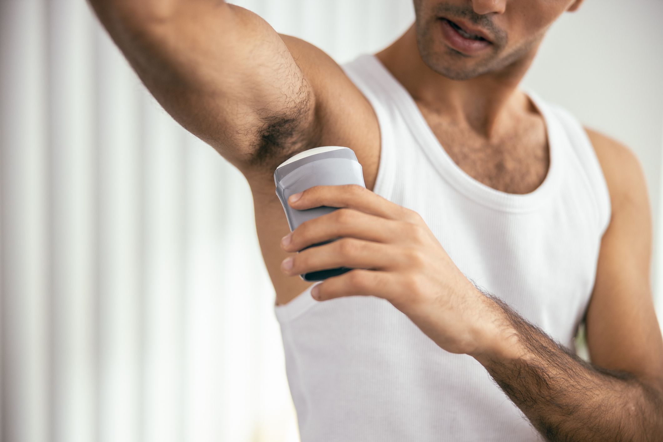 Young man applying deodorant to armpit at his apartment