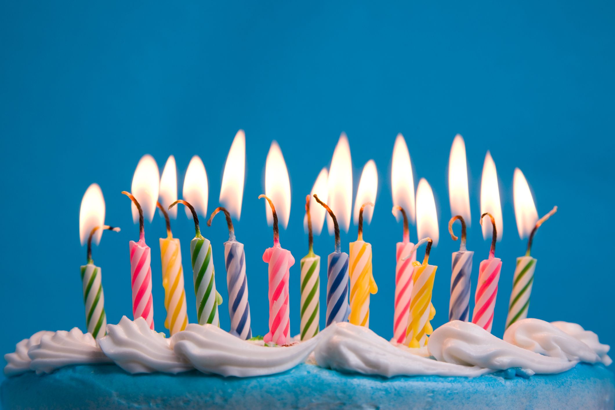 Close-up of flaming birthday candles on a cake against a blue backdrop