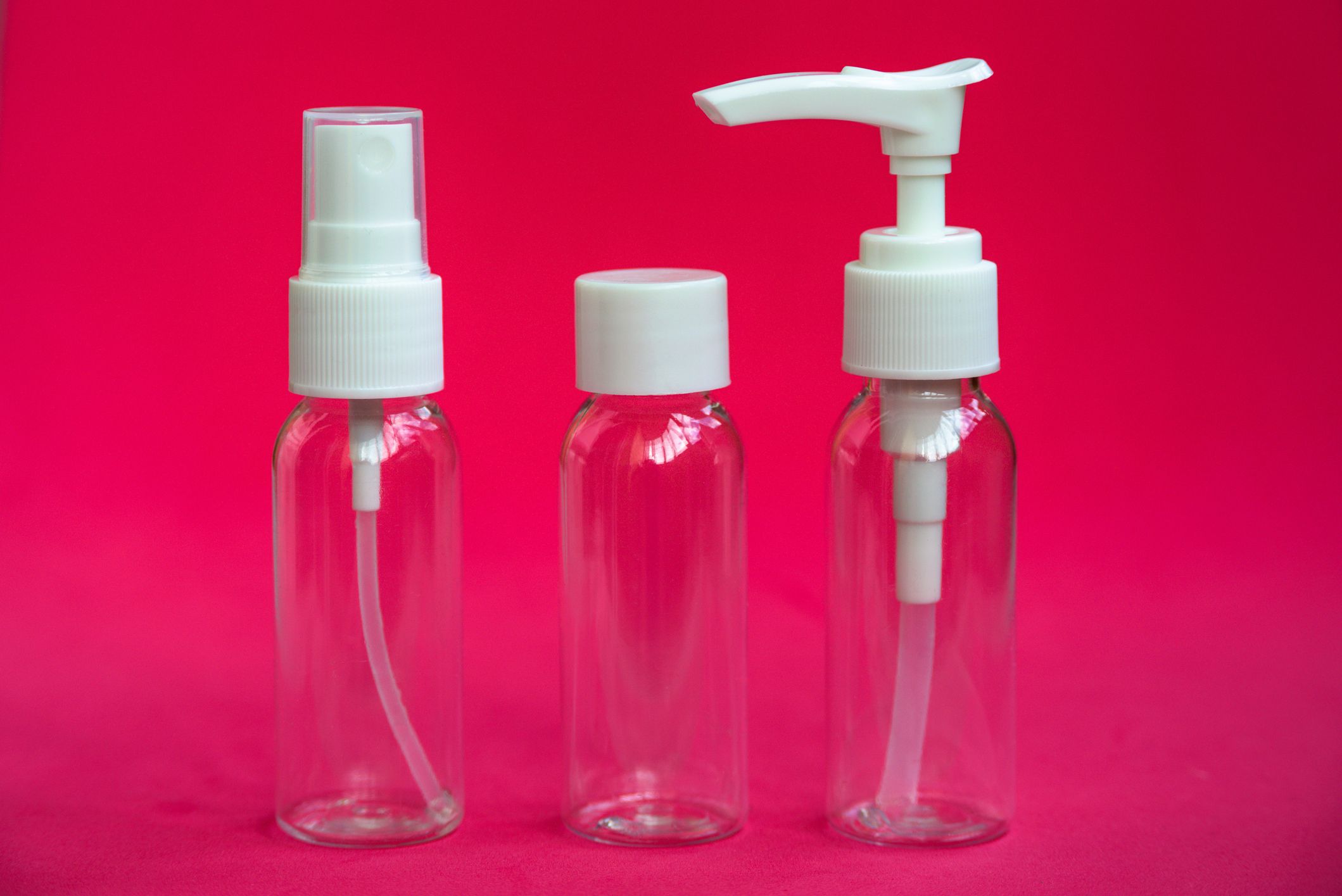 Set of empty small traveling cosmetics bottles on pink background