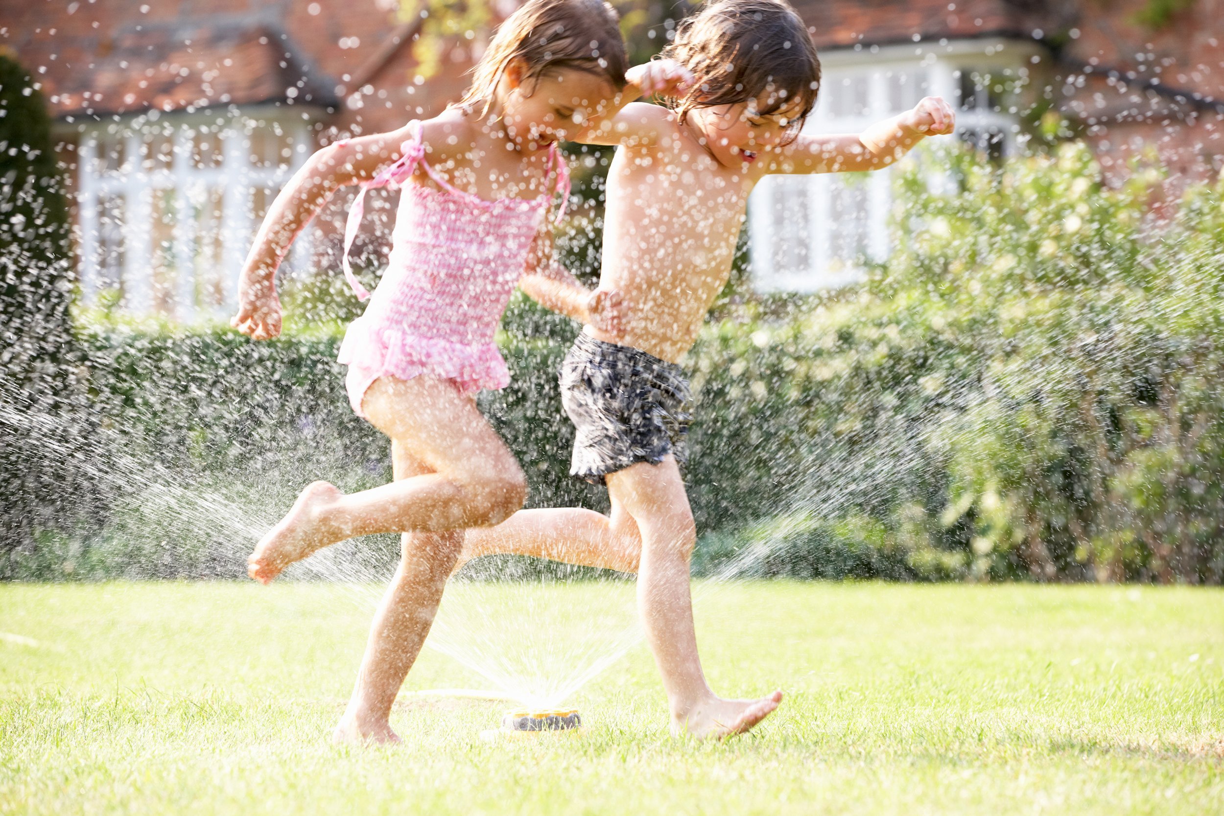 two children running through a sprinkler