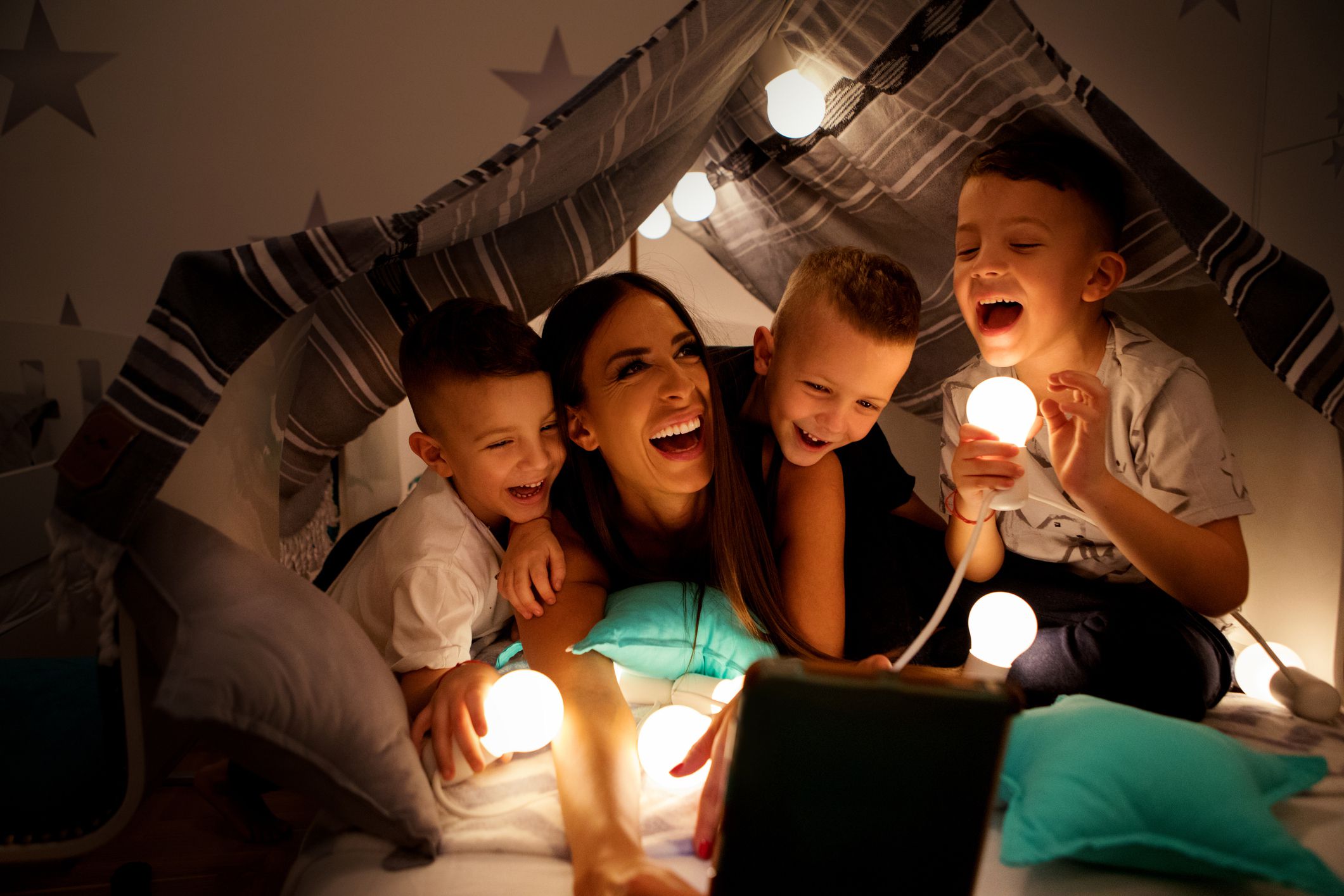 family in tent made of sheets and pillows with lights