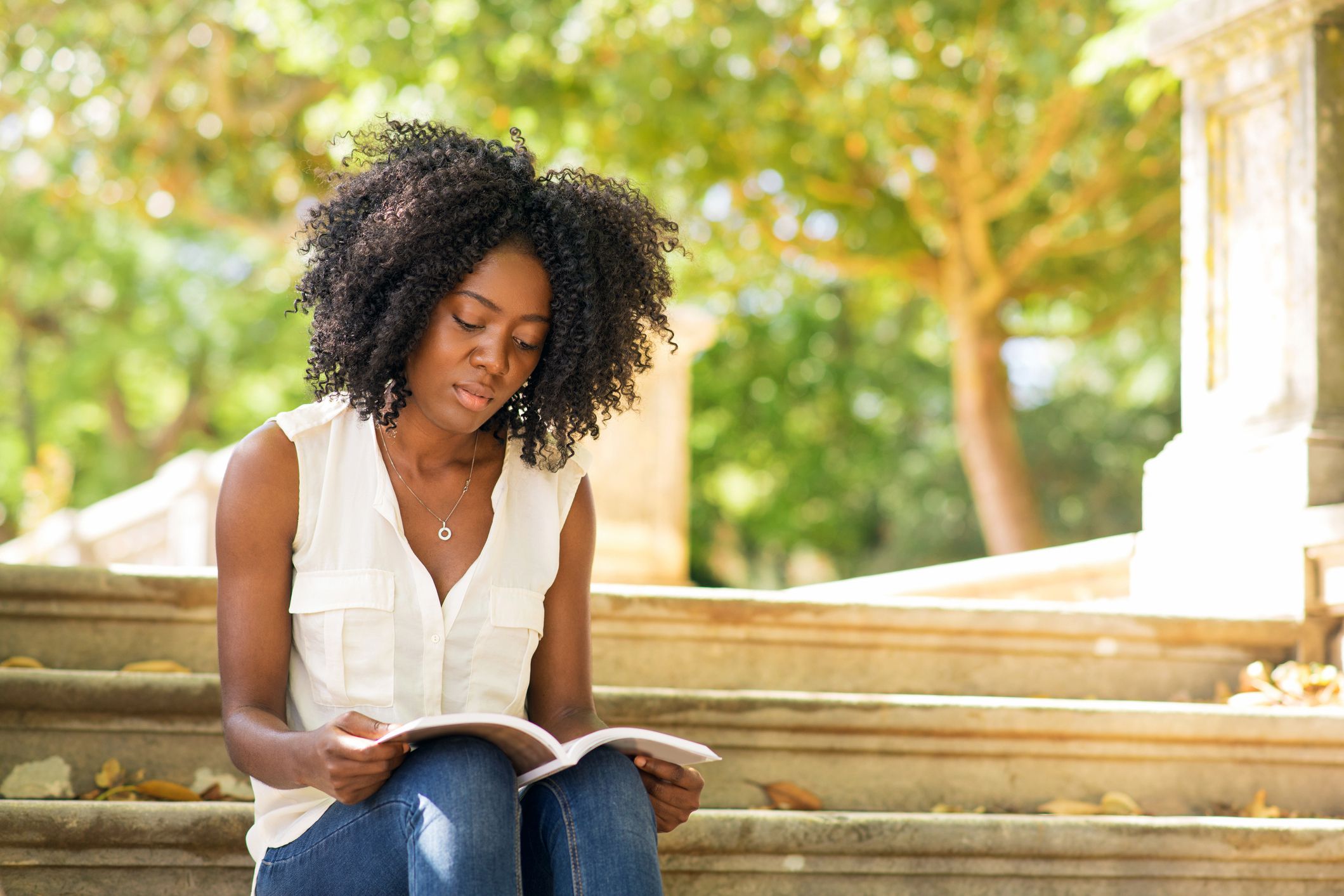 young woman reading a book on park steps